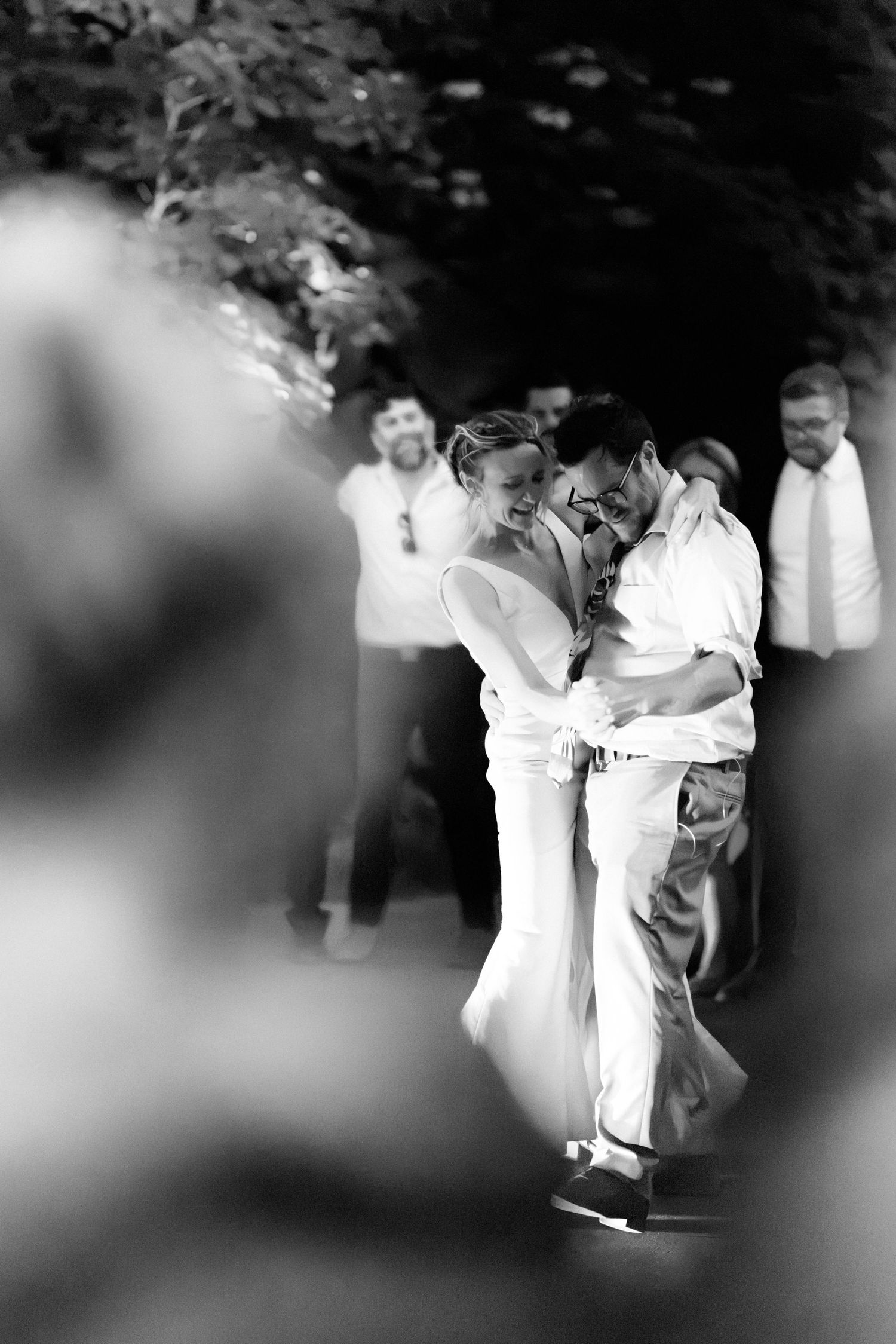 Black and white photo of laughing bride and groom sharing joyful embrace during outdoor wedding celebration.