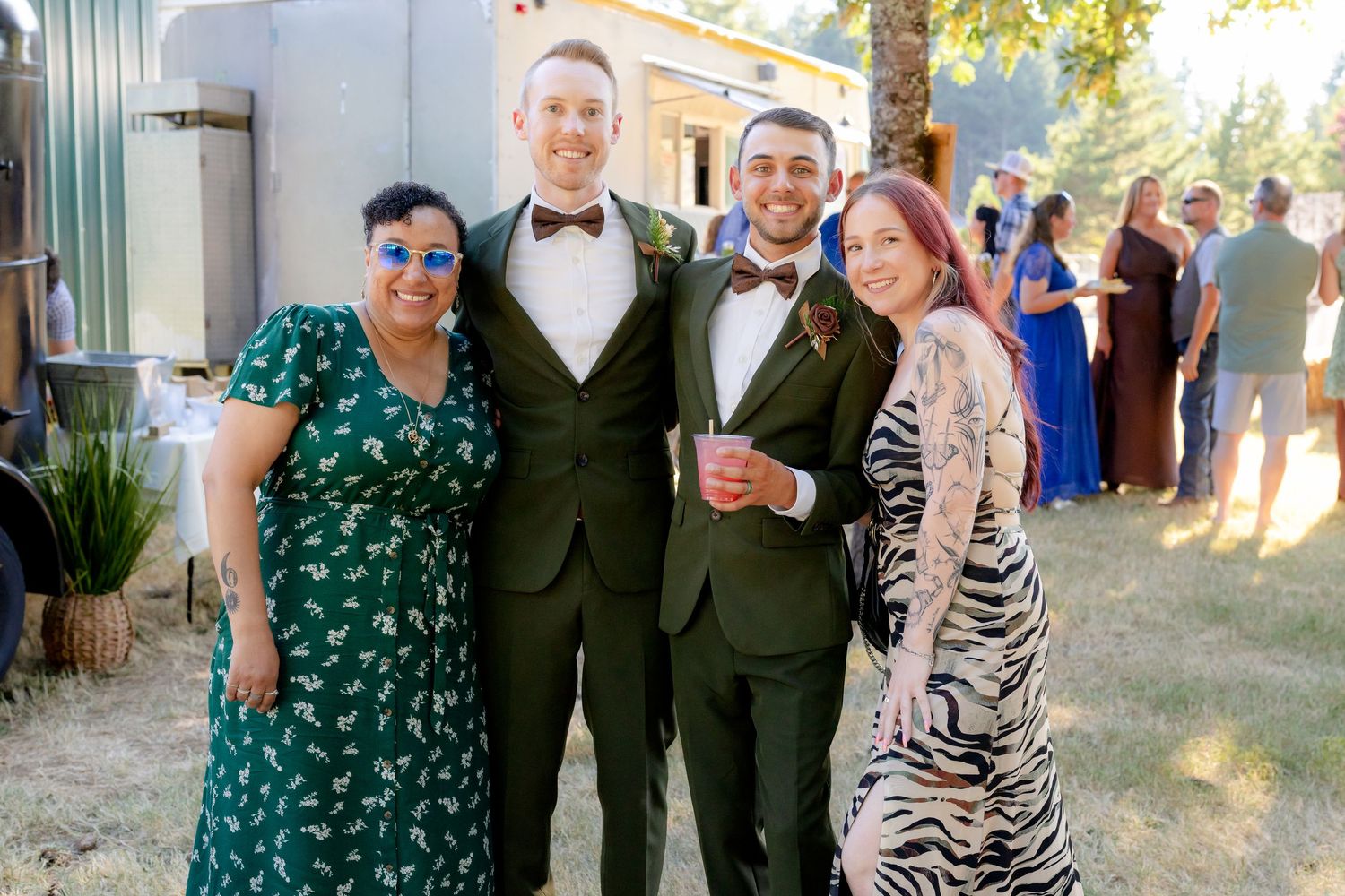 Group of four smiling guests posing together at an outdoor wedding reception near a silver trailer.