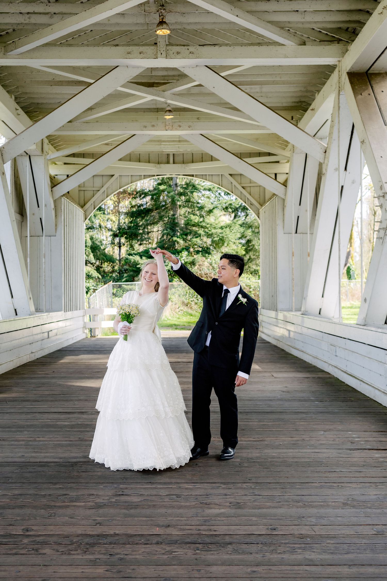 Bride and groom dancing inside a white covered bridge on their wedding day.