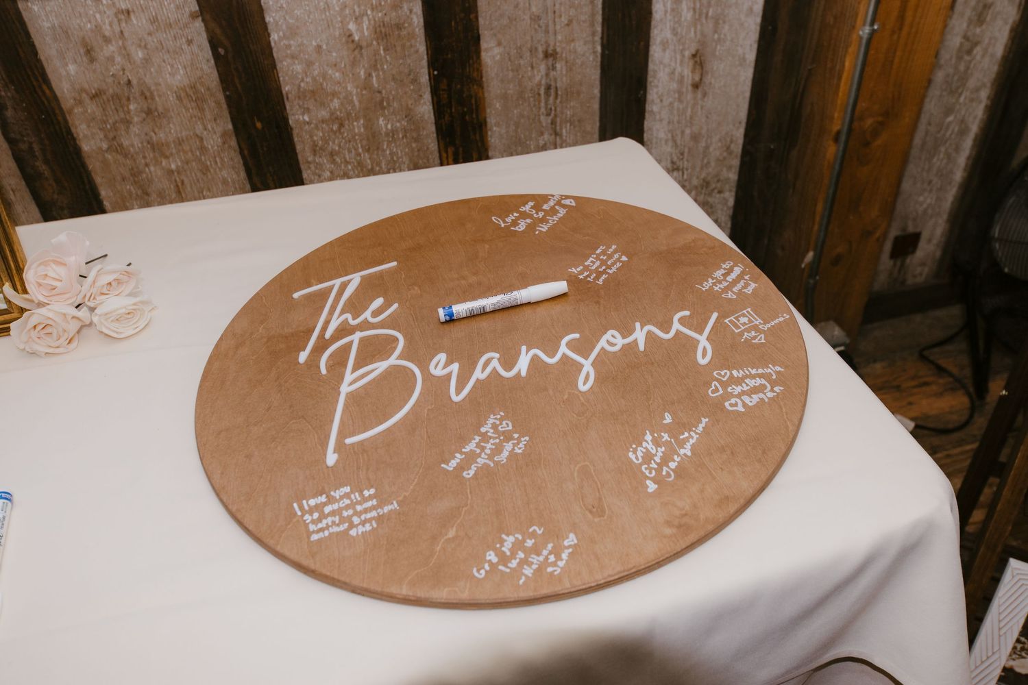 Round wooden guest book signed with white marker reading The Bransons on white table.