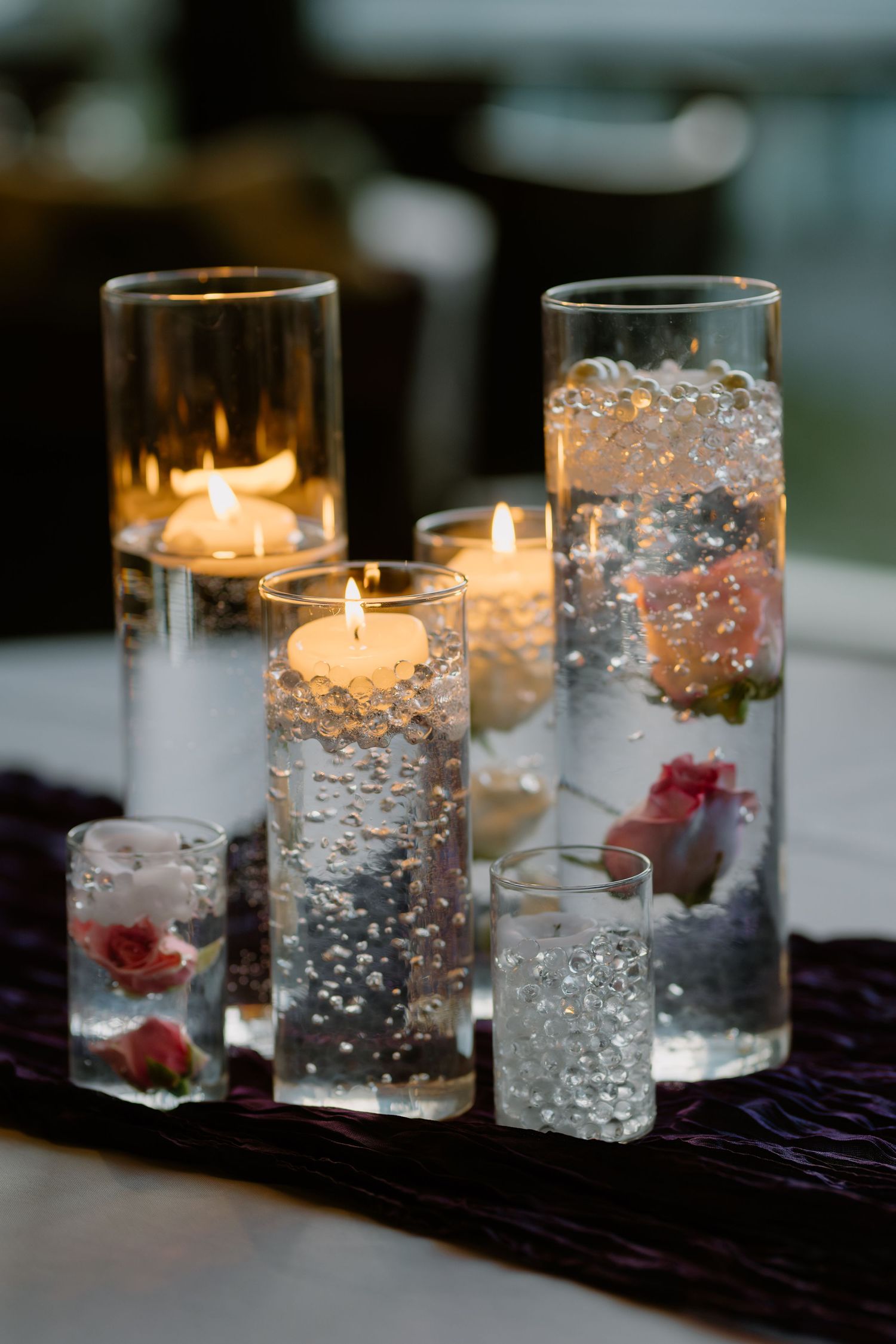 Elegant wedding centerpiece with floating candles in tall glass cylinders filled with water, bubbles, and submerged pink roses.