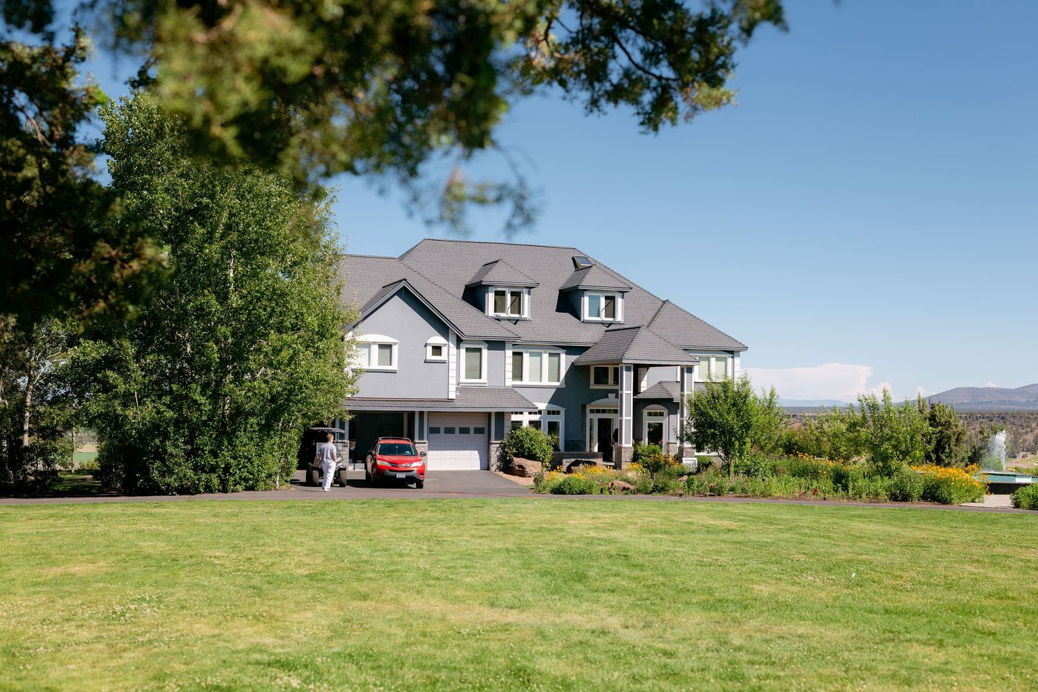 Large elegant two-story home with gray roof surrounded by lush green lawn and landscaping.
