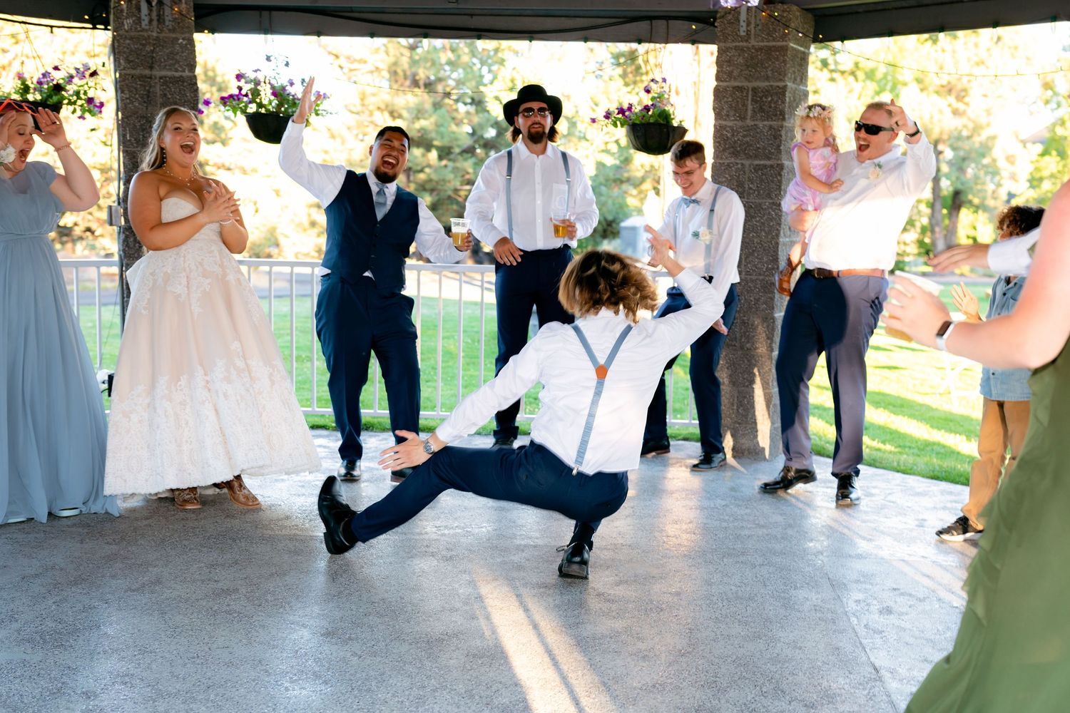 Energetic guest doing splits on dance floor at outdoor wedding reception under pavilion.