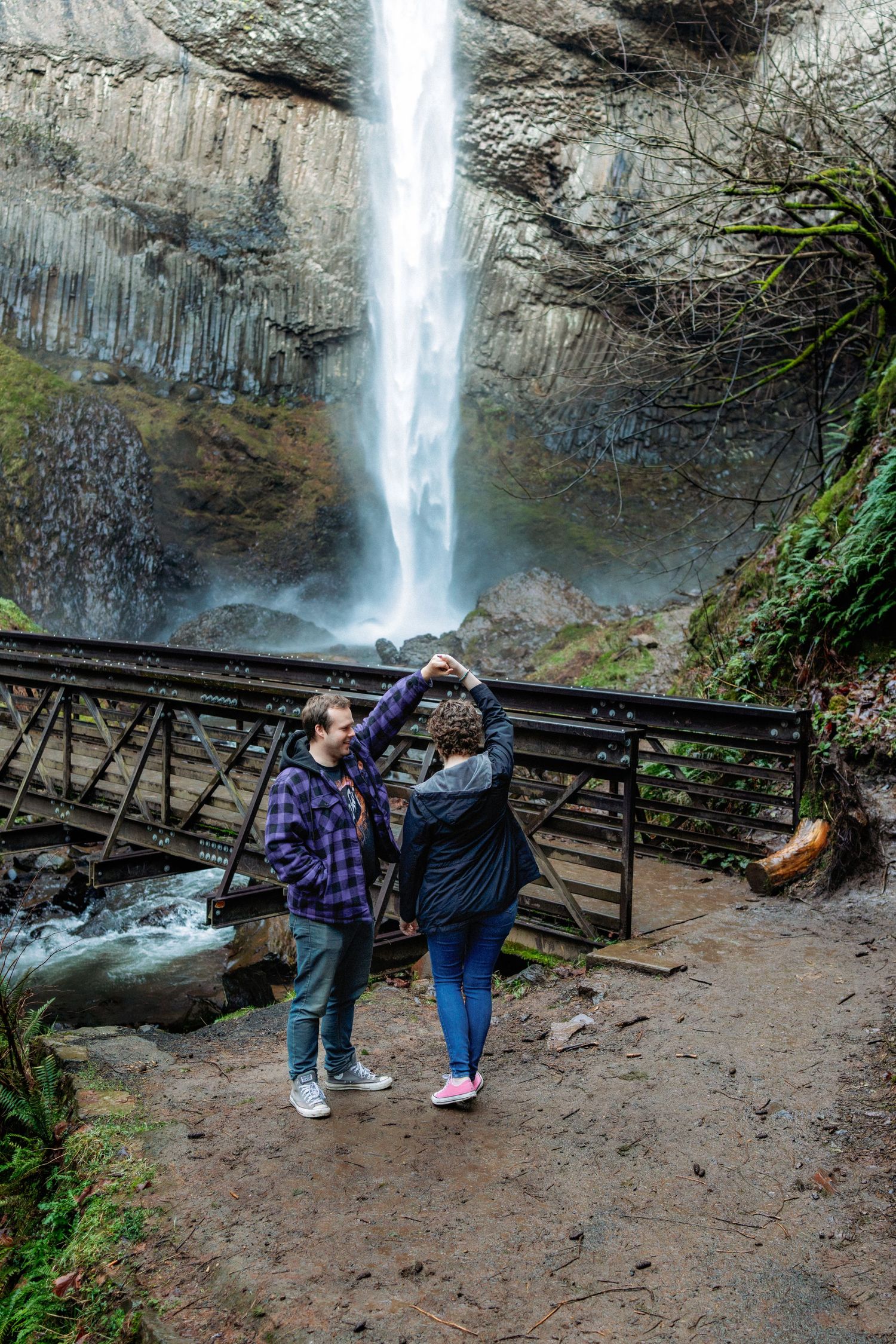 A scenic waterfall cascades down rocky cliffs with a wooden viewing platform visible in the foreground.