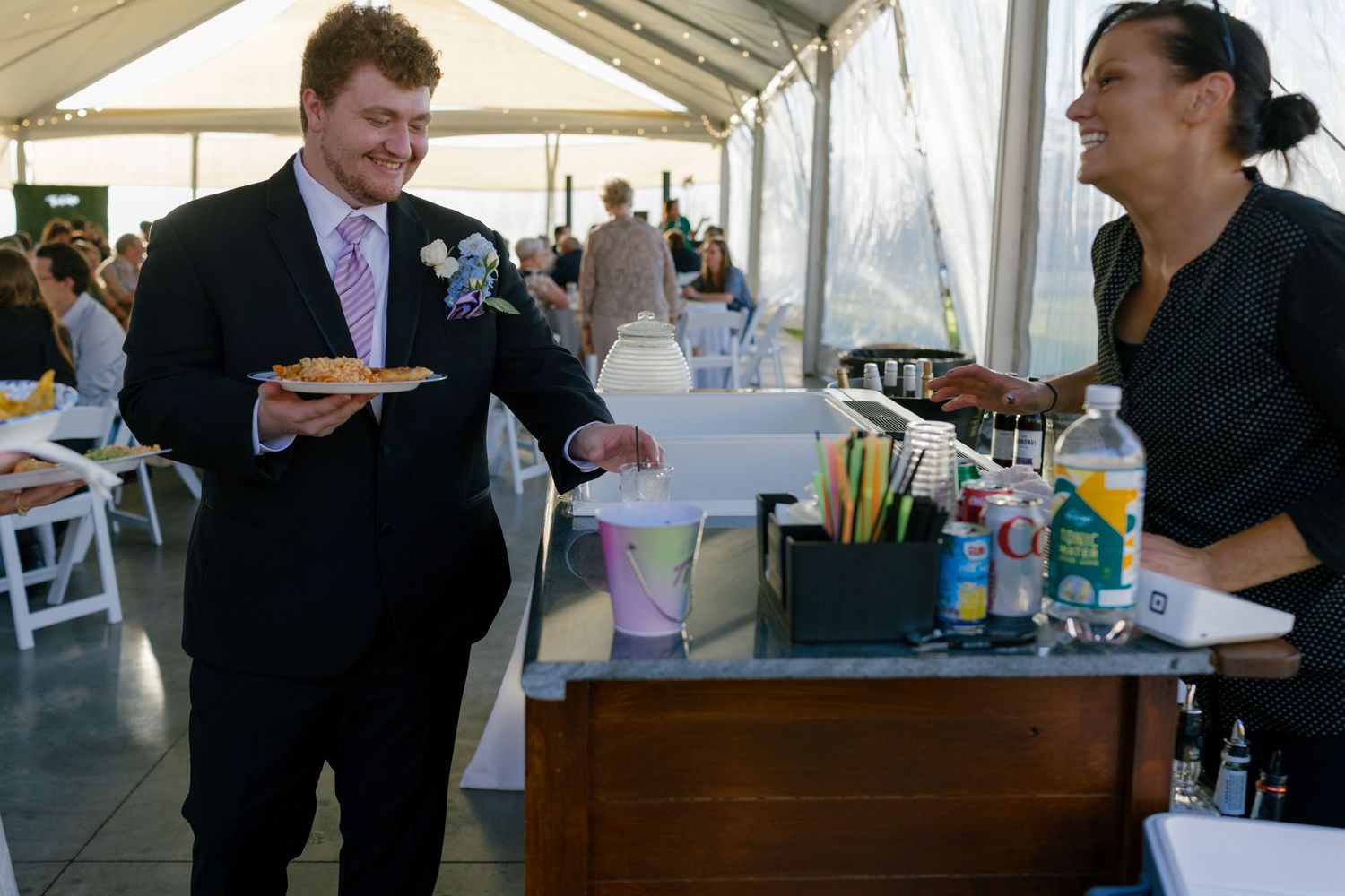 Wedding guests mingle and chat at a reception under a white tent.
