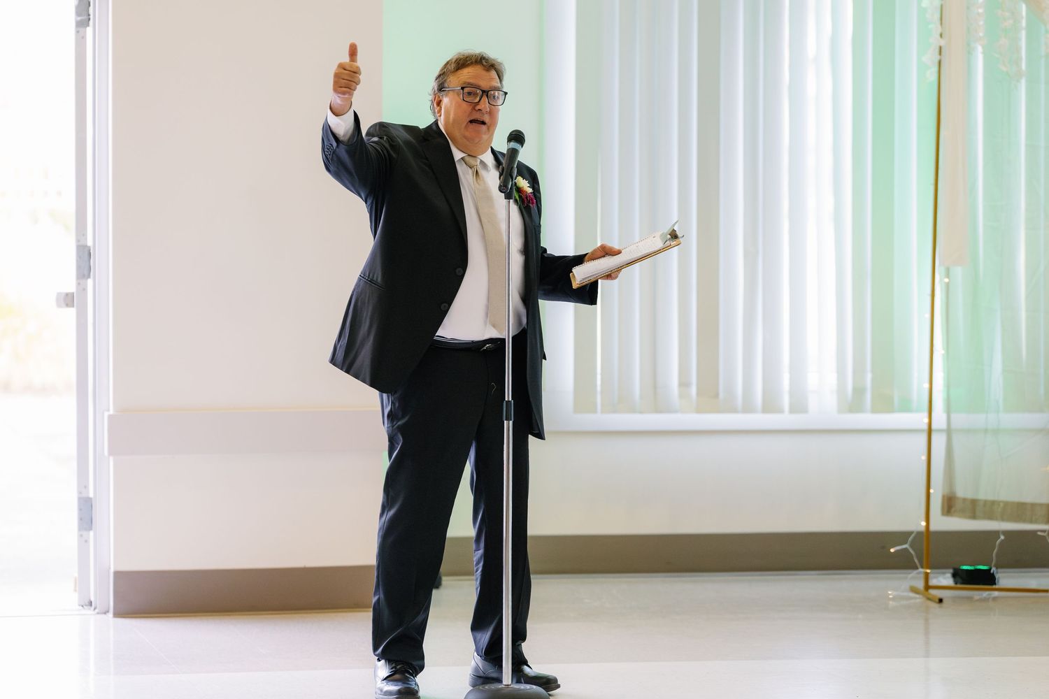 A speaker gestures while presenting at a podium in a bright room.