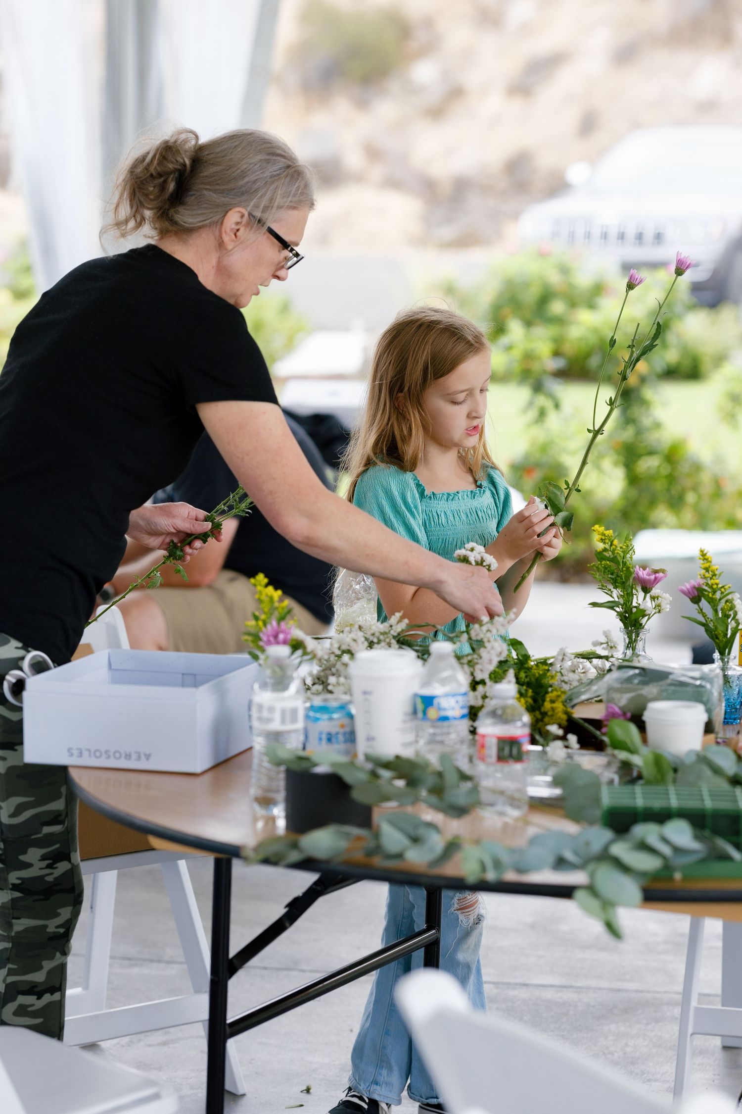 People gathered at a table participating in a floral arrangement workshop with flowers and greenery.