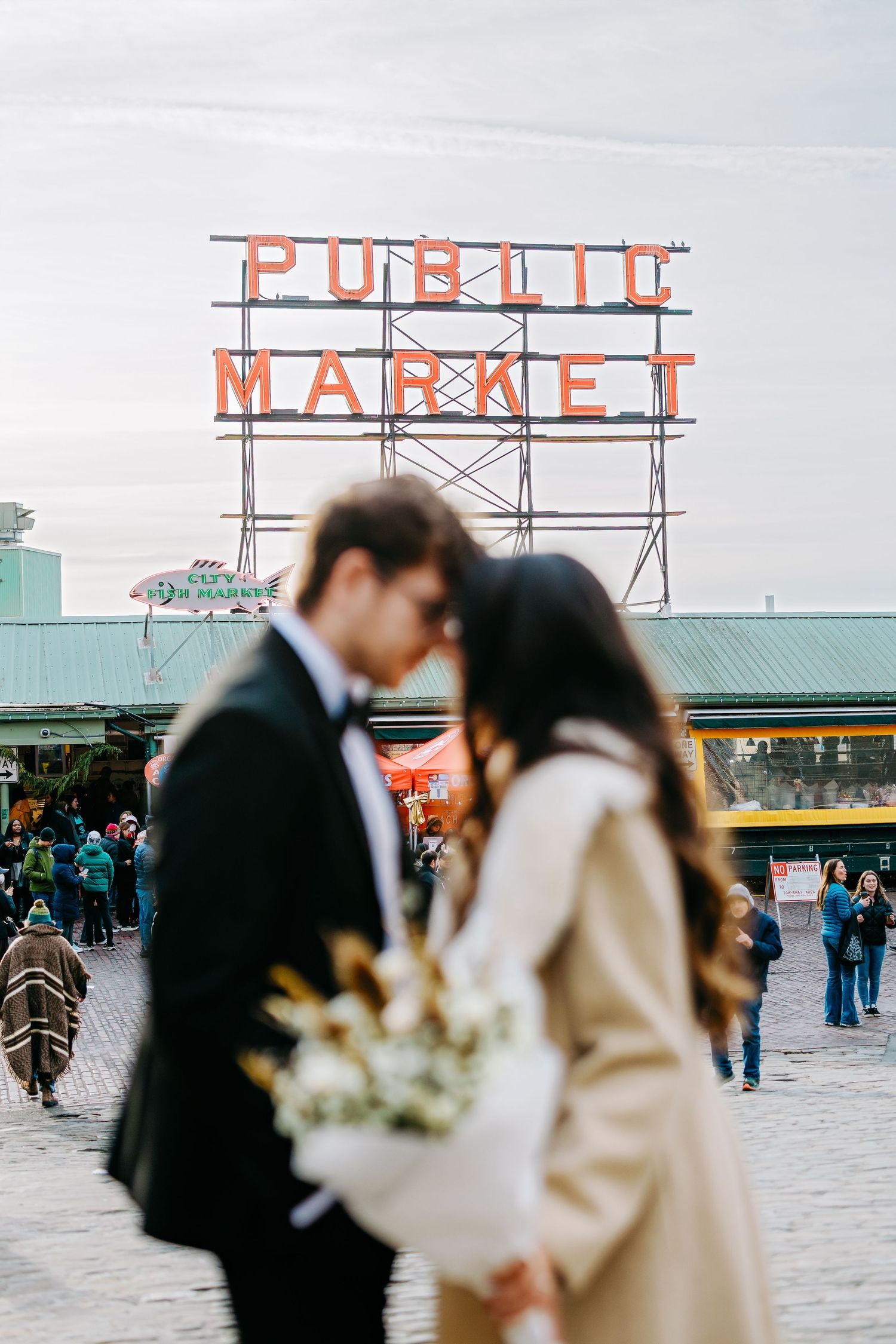 A couple shares a tender moment in front of the iconic Pike Place Market sign.