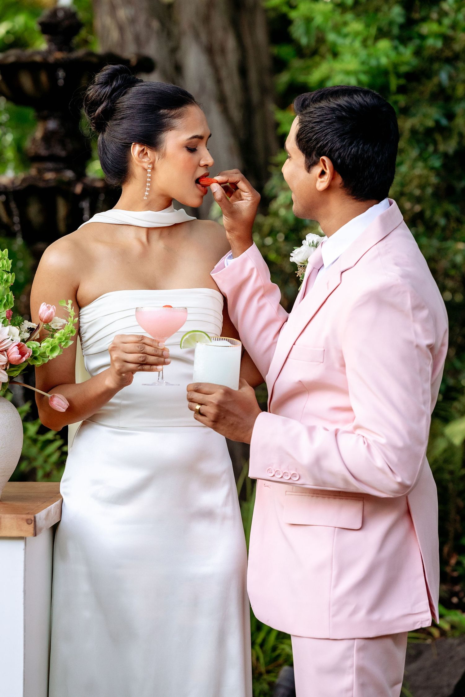 A couple in white and pink attire shares an intimate moment while holding cards during an outdoor photo session.