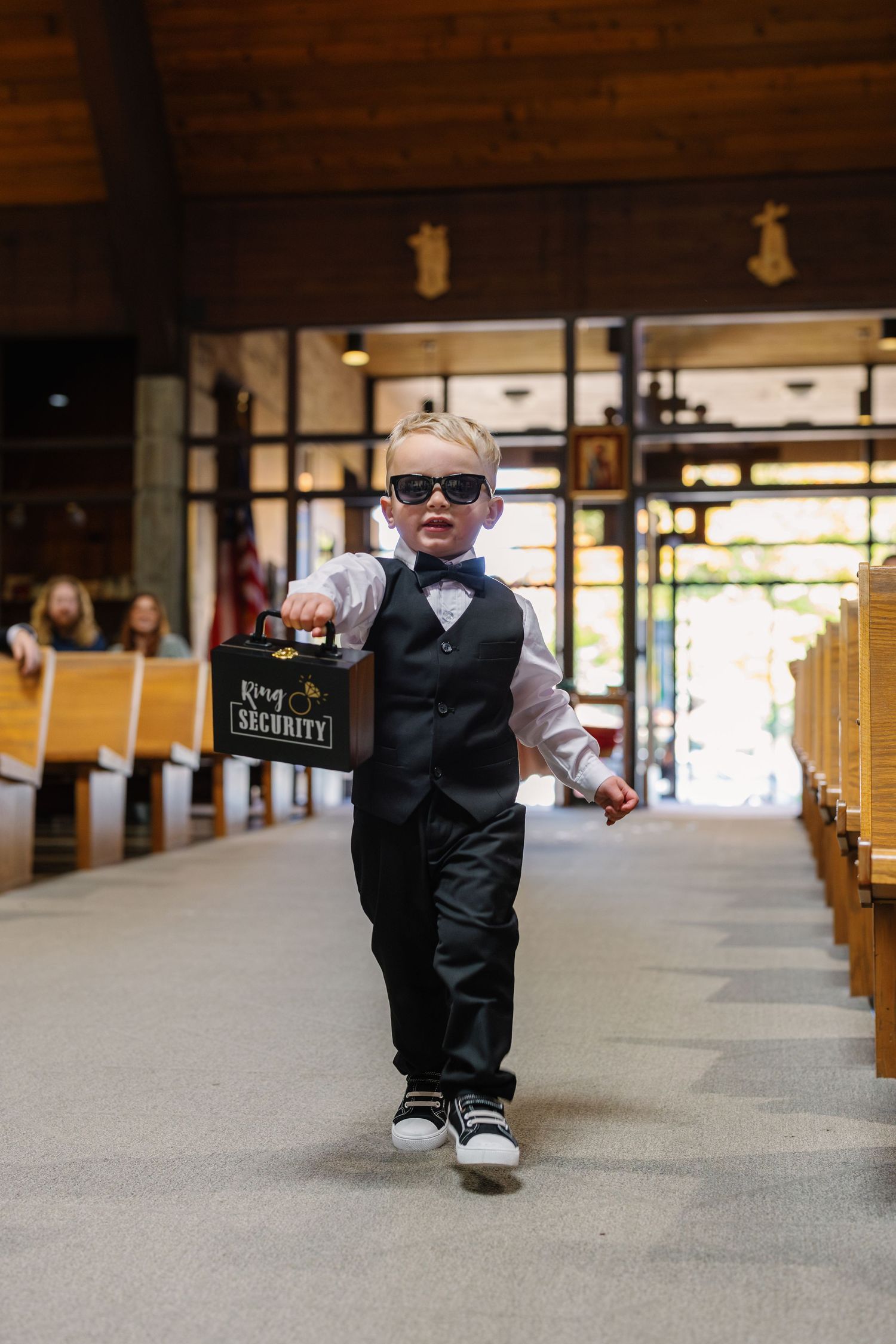Small child in formal attire walking down church aisle during wedding ceremony.