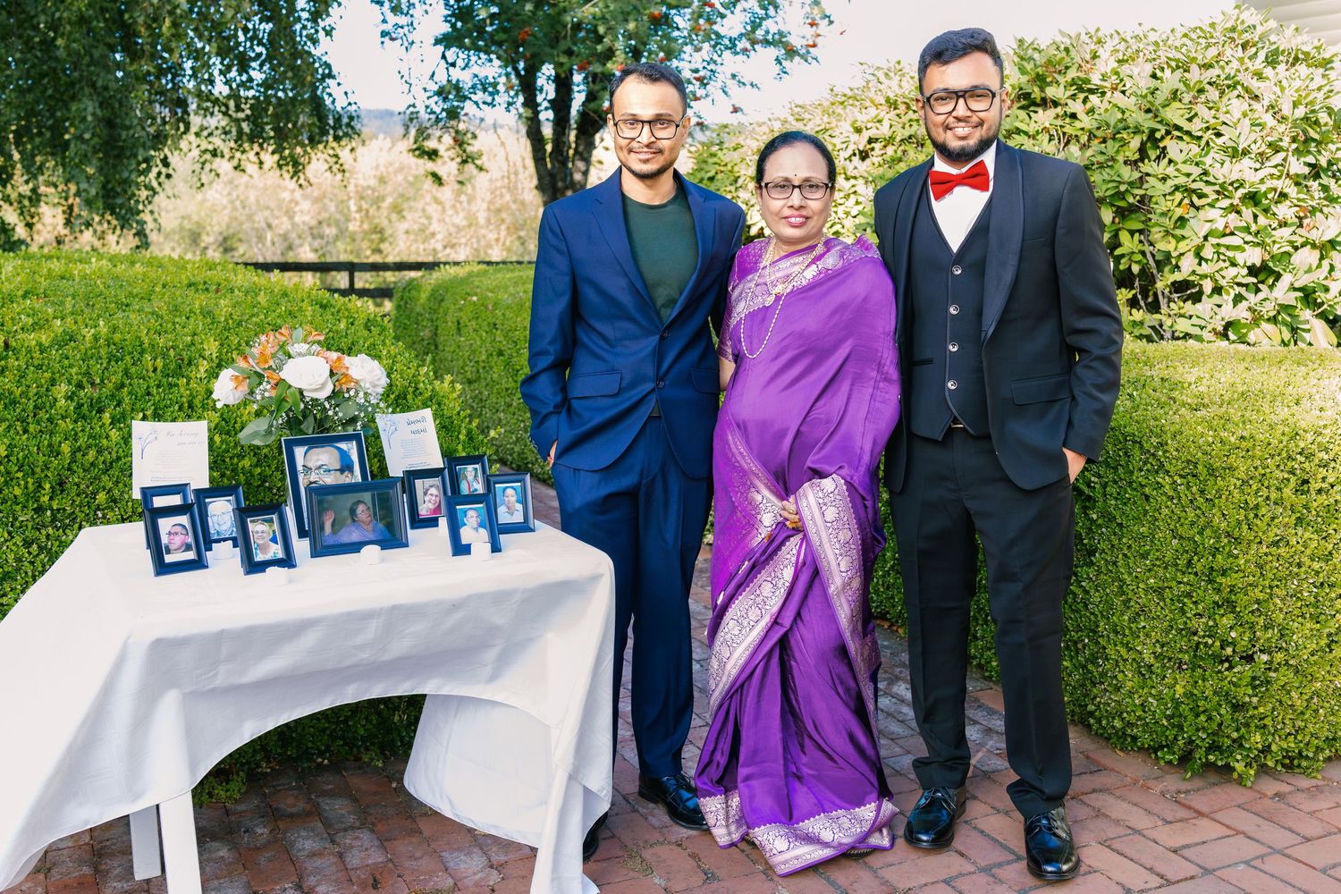 Wedding party poses for formal portraits on brick pathway surrounded by greenery.