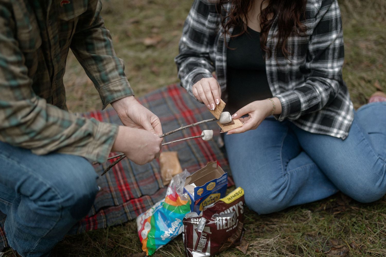 A person sitting on a plaid blanket outdoors sorting through colorful candies and snacks.
