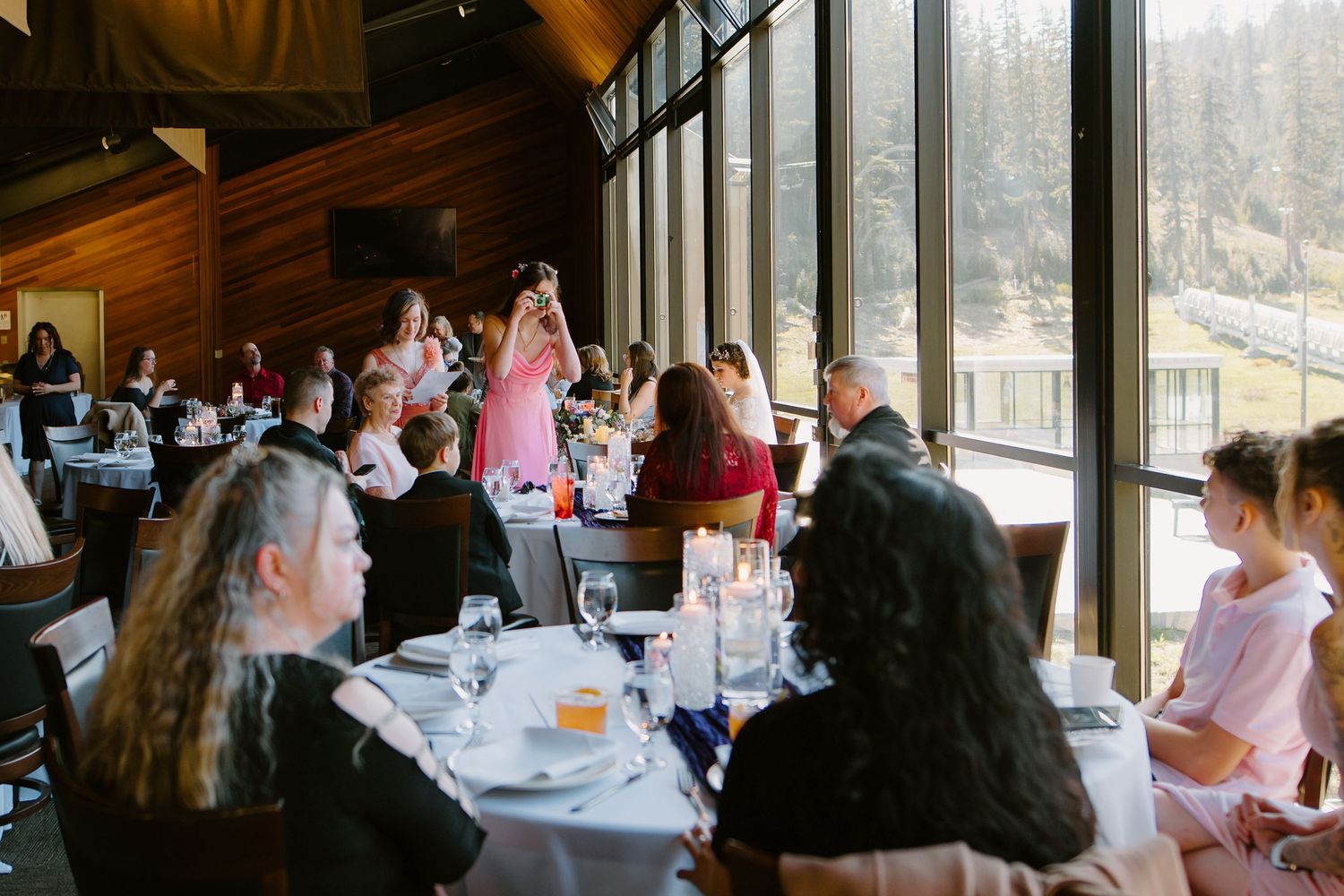 Guests dining at elegant restaurant with floor-to-ceiling windows overlooking scenic views during a special event.
