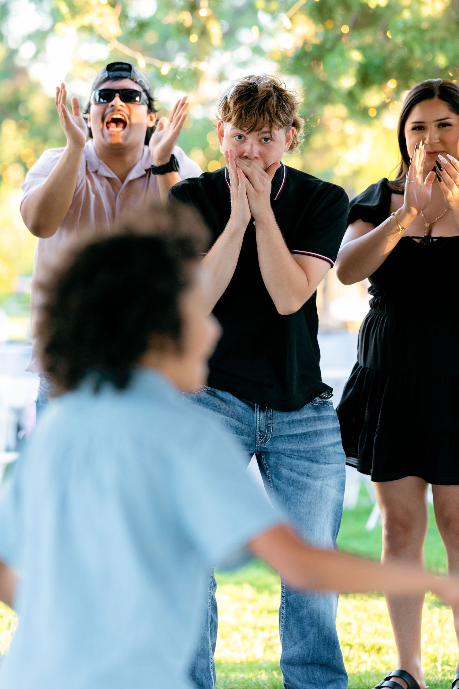Excited guests cheering and clapping for a child during an outdoor park gathering.