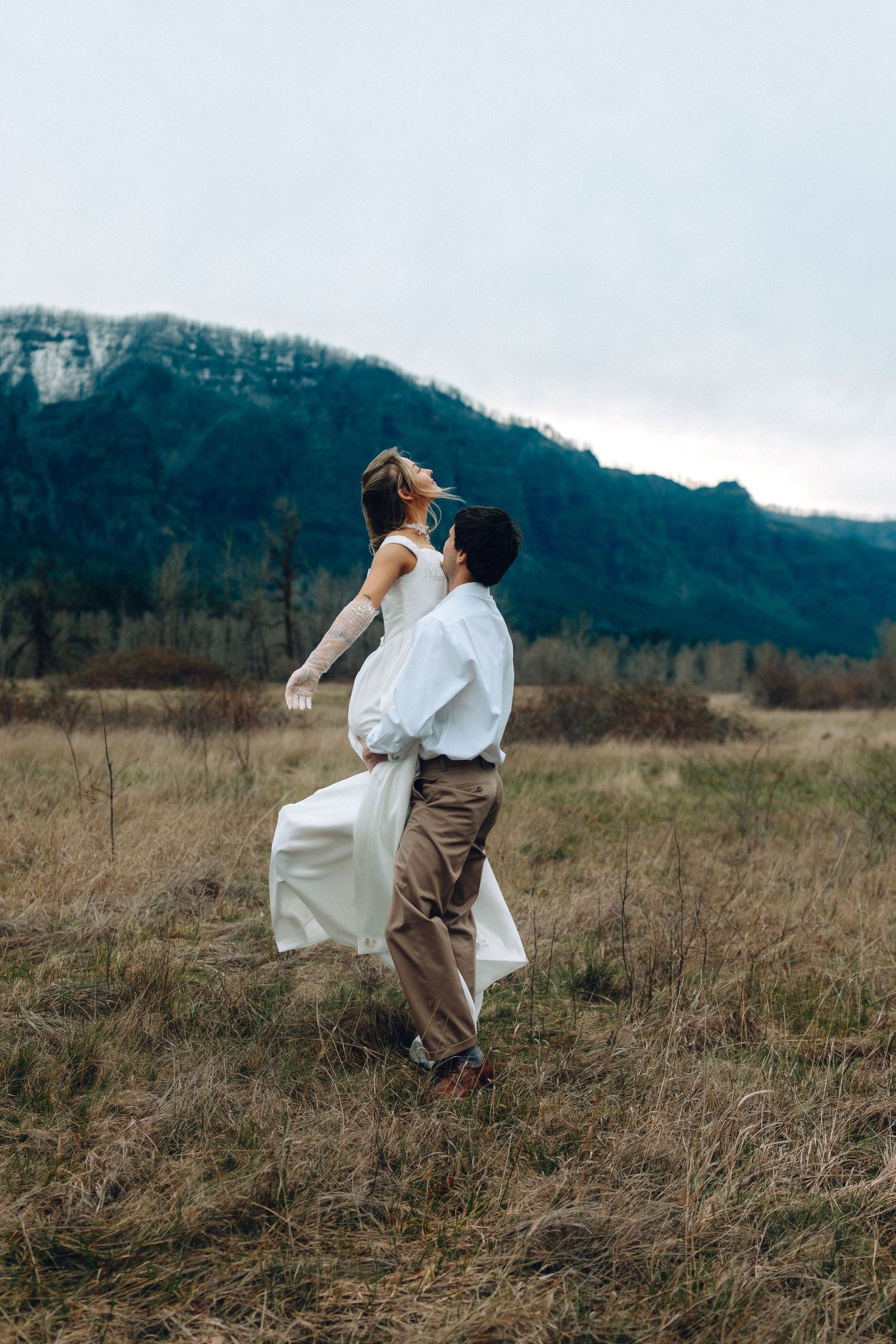 Artistic wedding photos of couple dancing in a field with mountains in the distance.