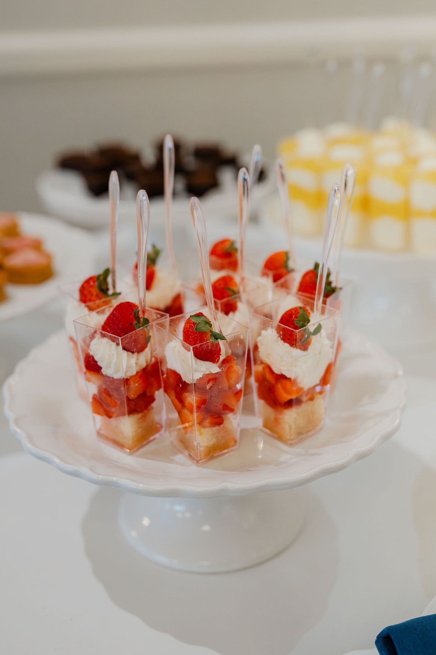 Elegant dessert cups with fresh strawberries and whipped cream on a white cake stand at a wedding reception.