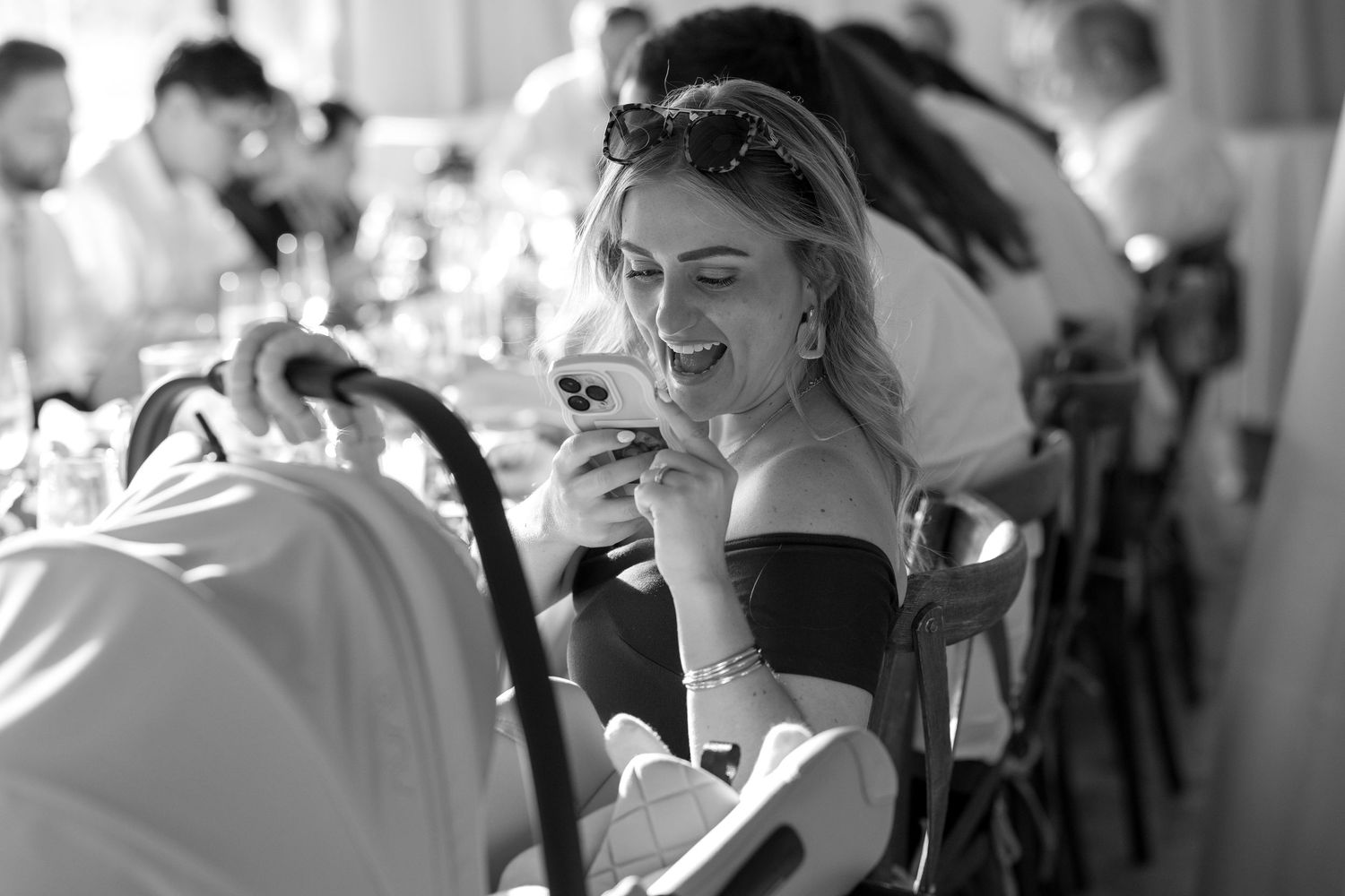 Black and white photo of an elegant guest at a formal dinner event wearing an off-shoulder dress and smiling.