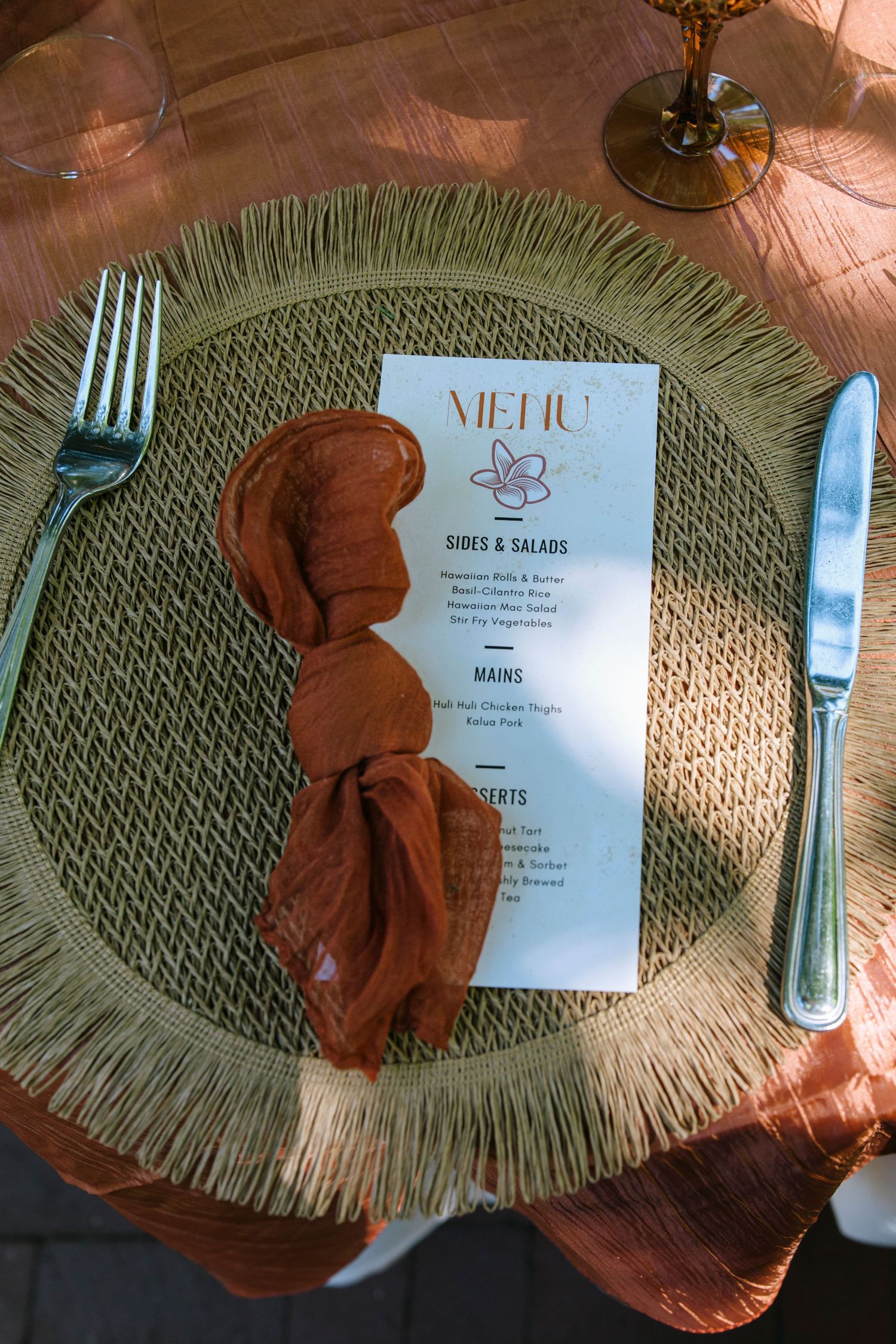 Wedding reception place setting with rustic woven placemat, terracotta napkin and elegant menu card.