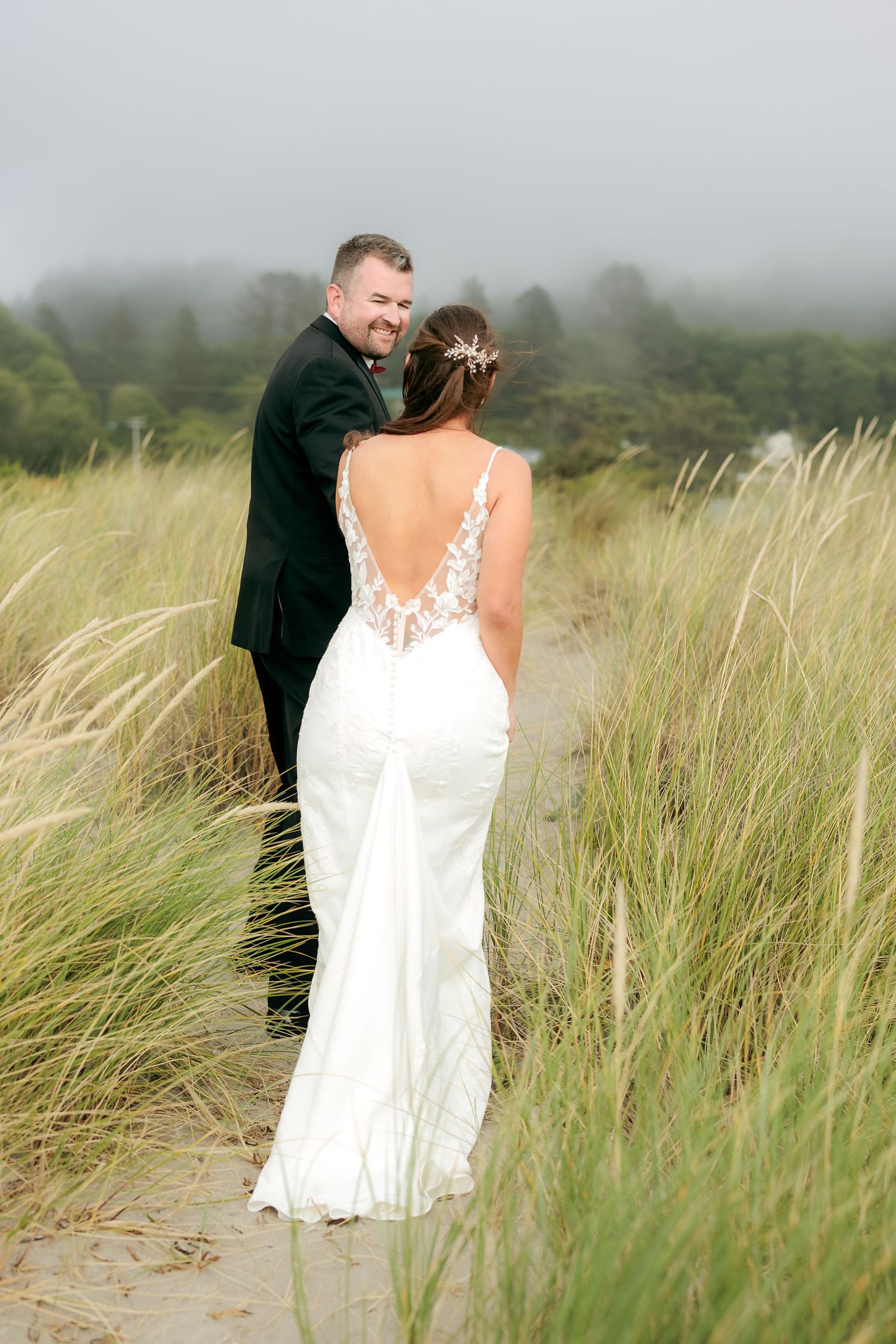 Wedding portrait on beach with elegant white dress detail and sea grass in foreground.
