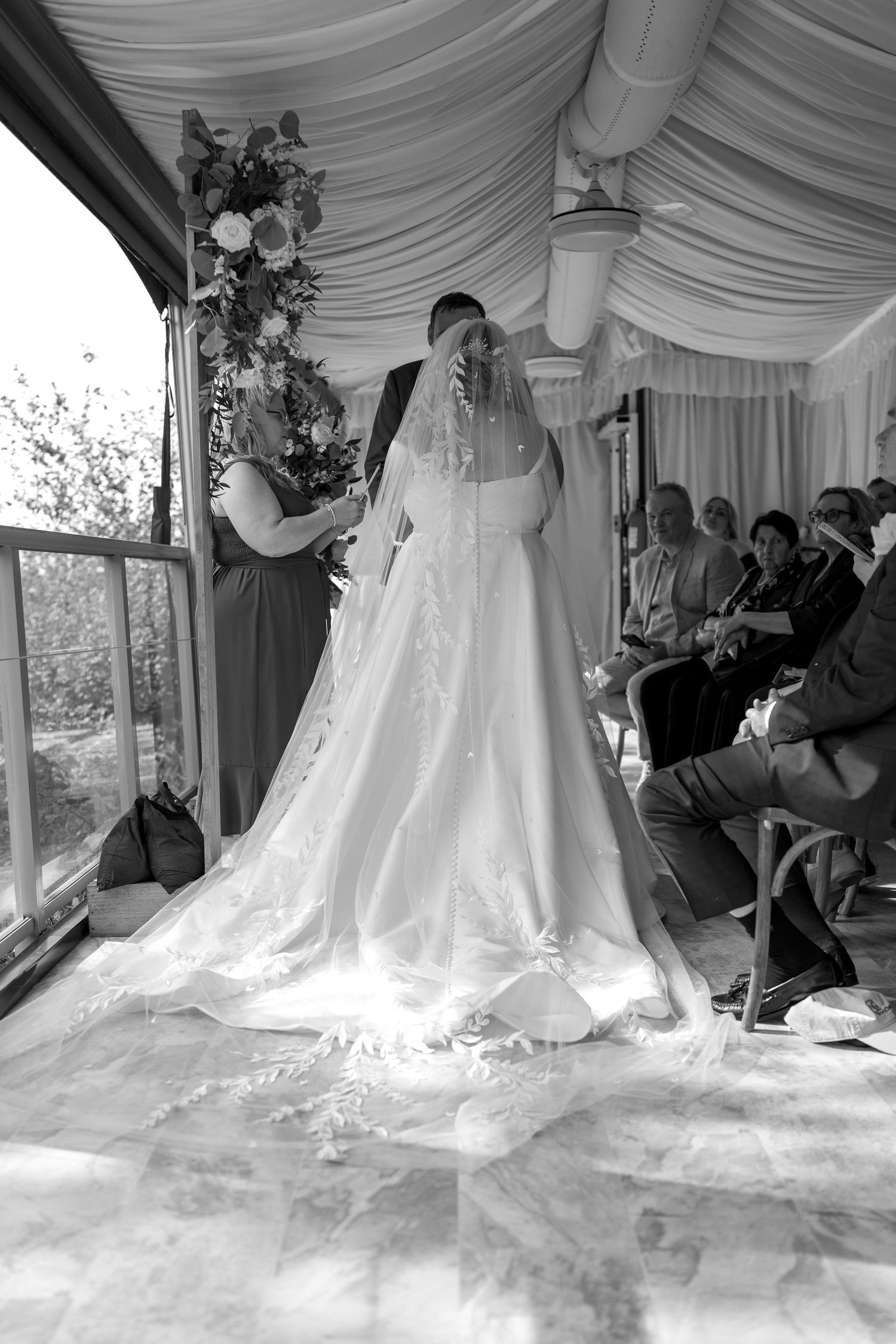 Wedding dress being bustled and arranged by attendants under an elegant white draped tent.