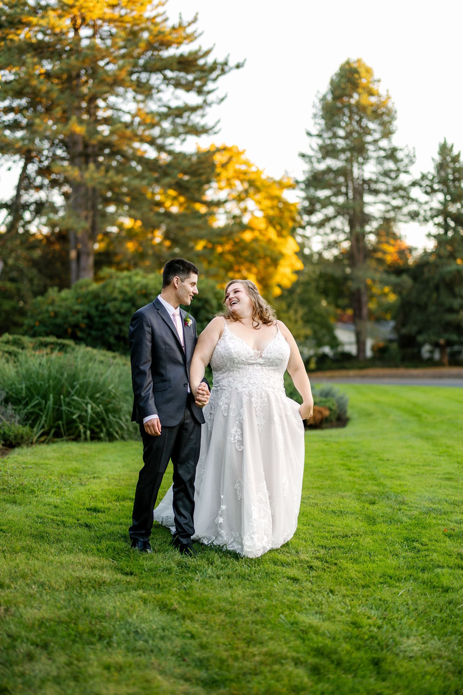 A couple poses together on a lawn with beautiful fall foliage in the background.