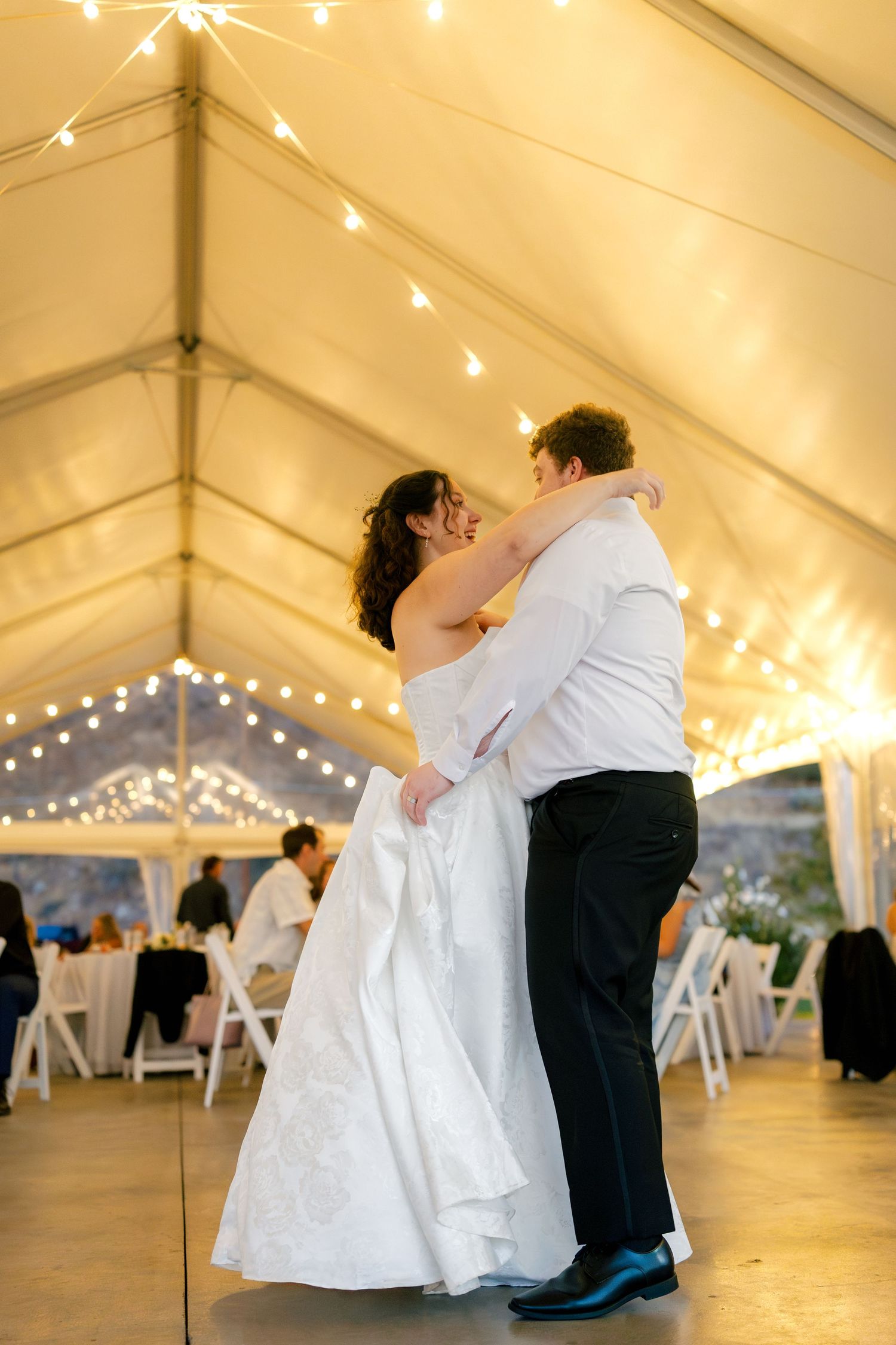 Romantic first dance at a wedding reception under a white tent with twinkling lights creating a magical atmosphere.