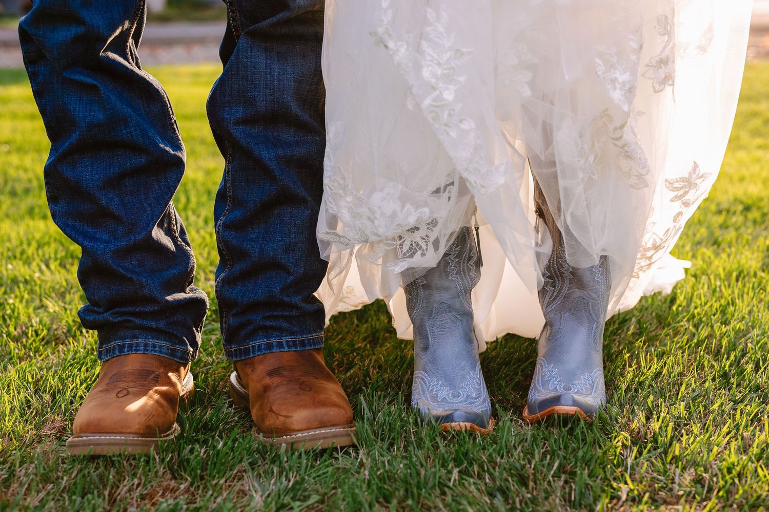 A line of wedding attendees' feet and shoes standing on grass, showing a mix of formal footwear and jeans.