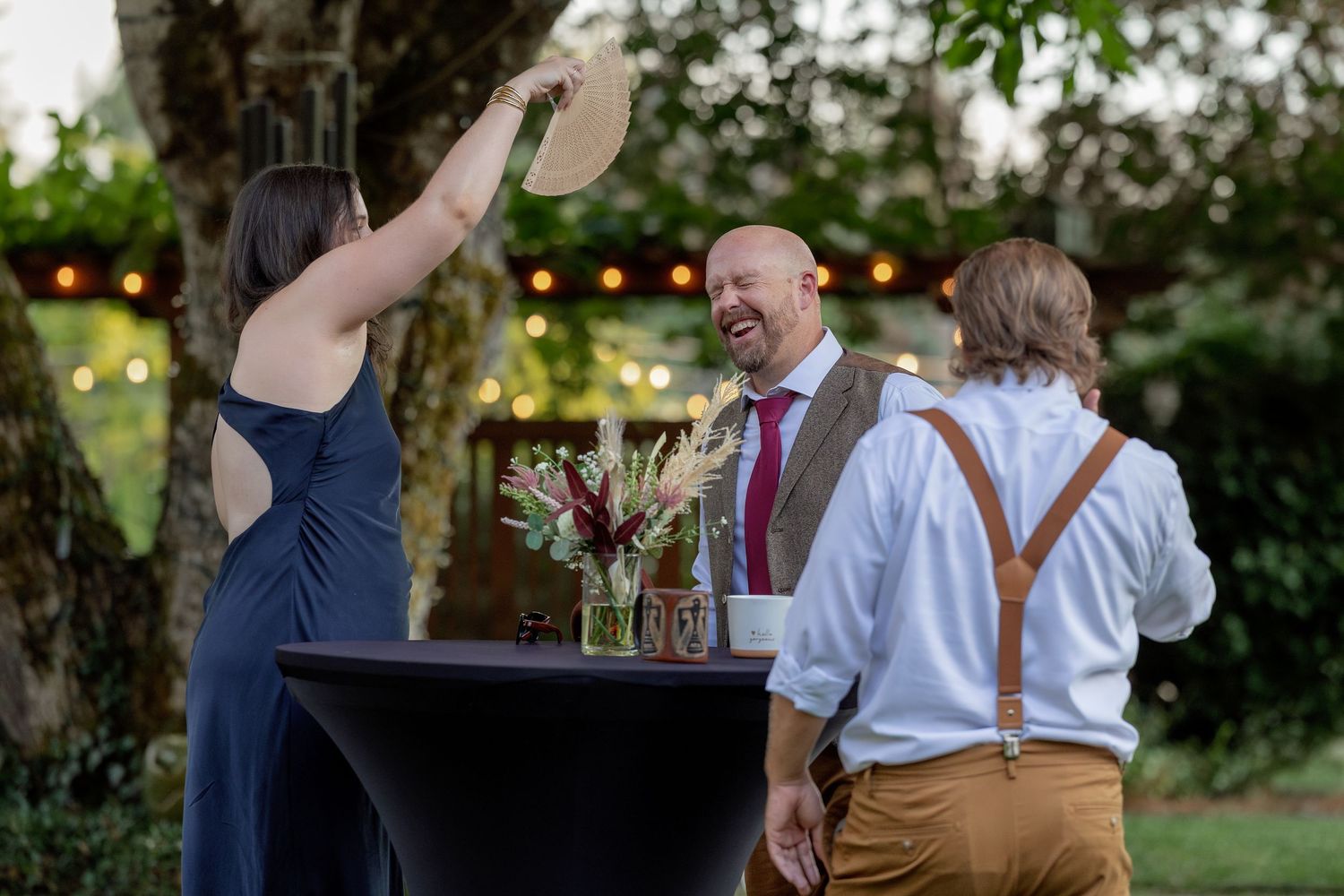 Casual outdoor wedding reception with guests mingling near a cocktail table.