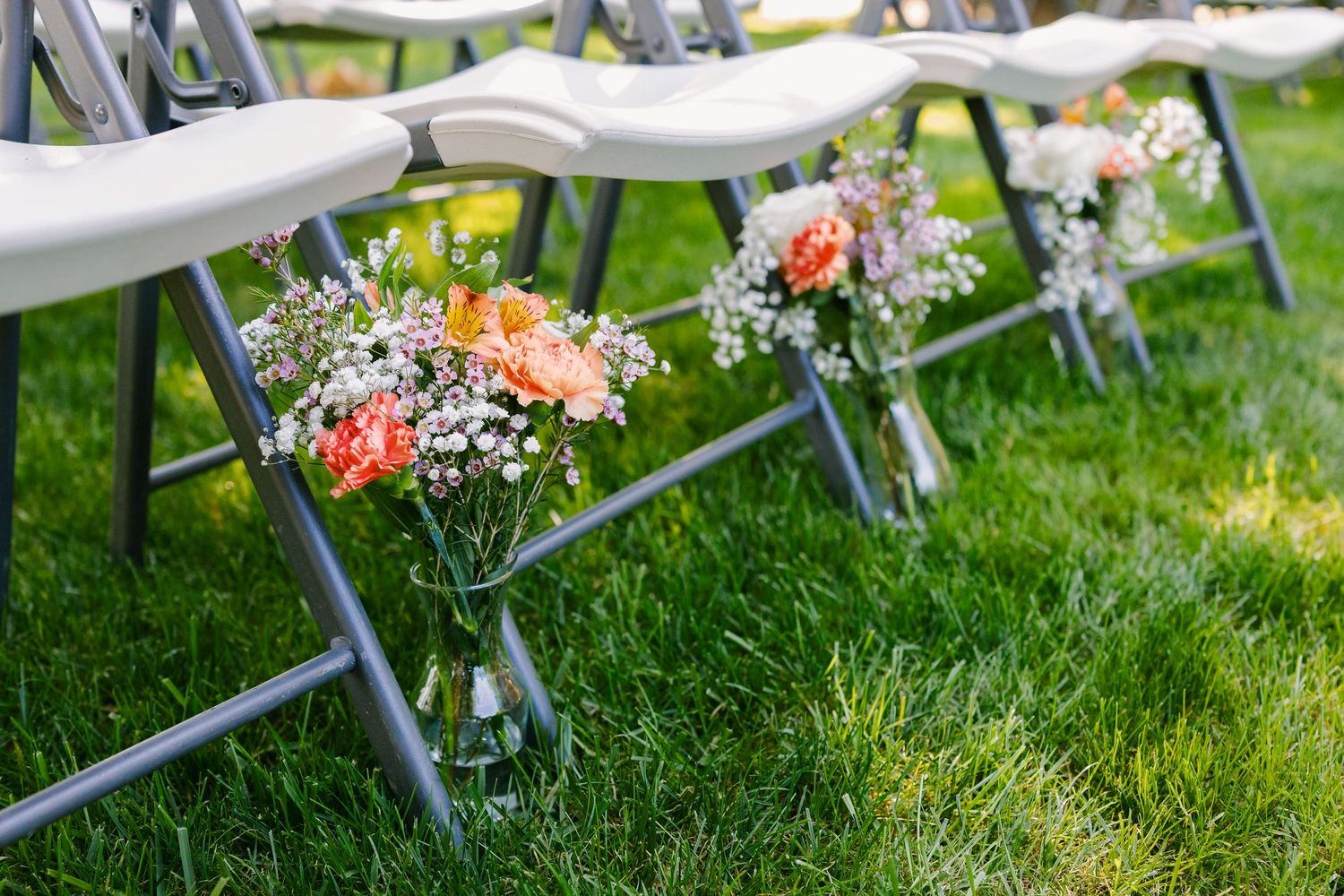 Elegant outdoor wedding reception setup with white chairs and floral arrangements on a lush green lawn.