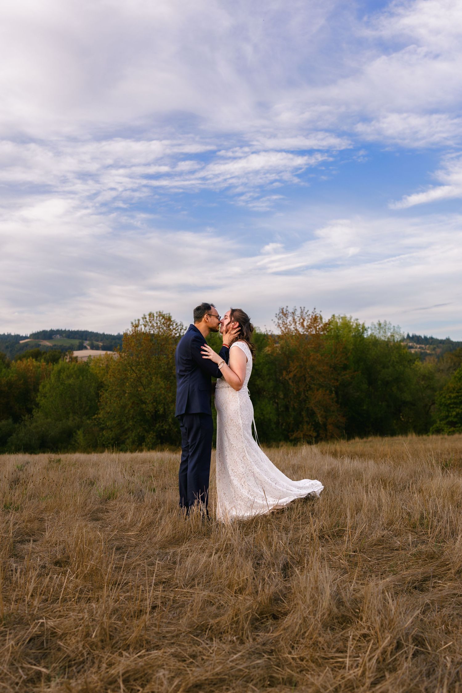 A couple shares a romantic moment in a golden field with mountains and cloudy skies in the background.