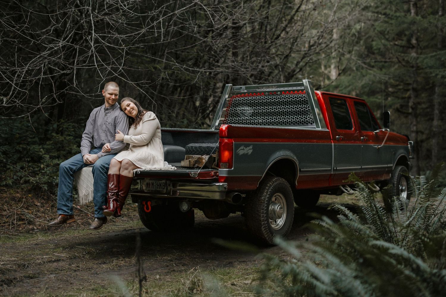 A couple sits together on rustic wooden stairs in a moody forest setting during an engagement photoshoot.