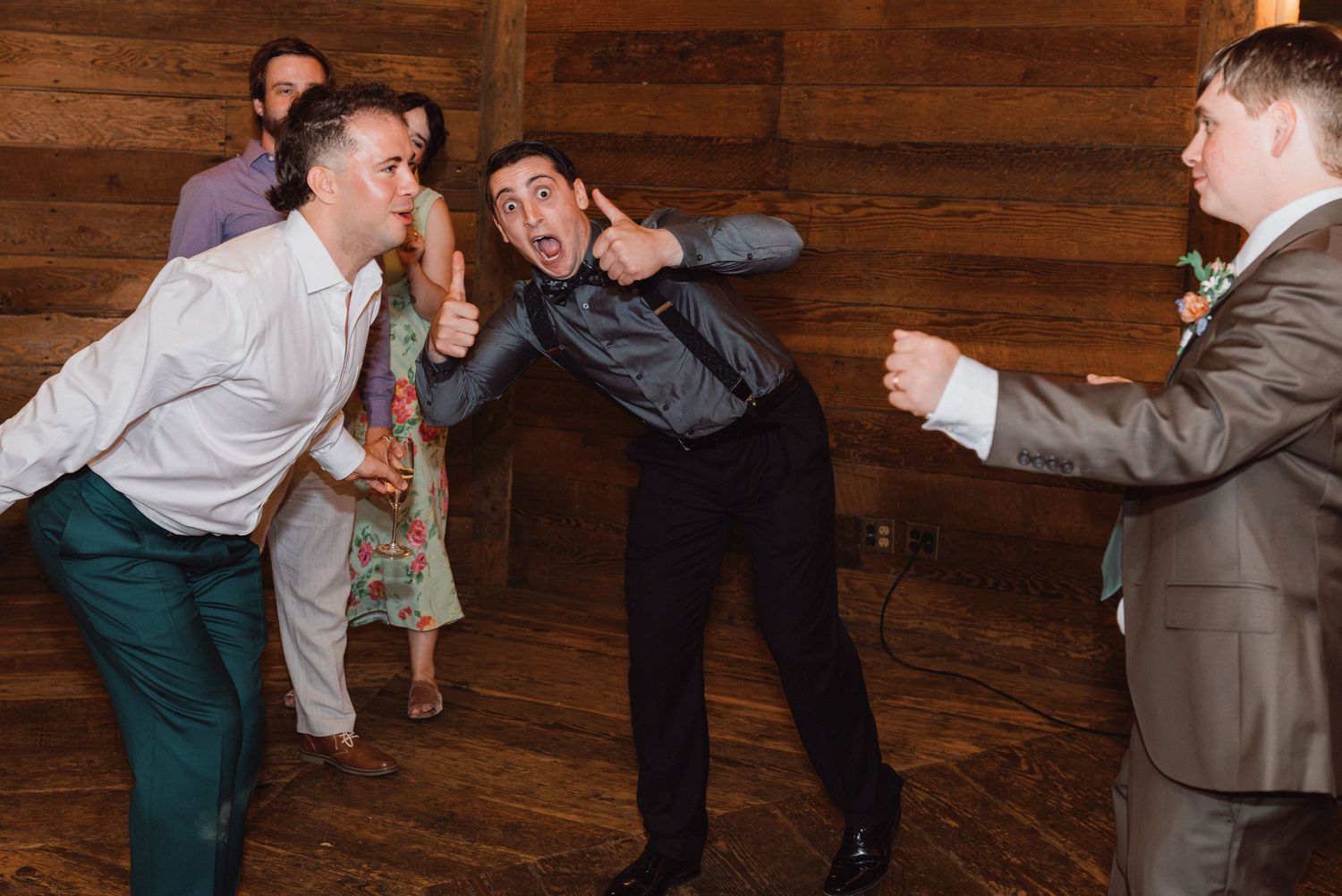 Guests dance energetically on a wooden dance floor at a lively indoor wedding reception.