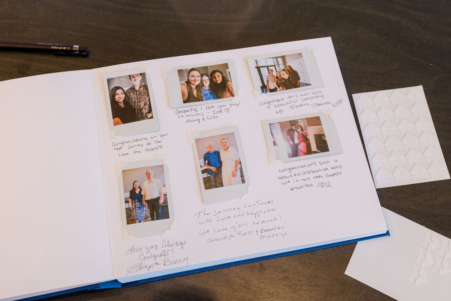 Wedding guest book open with Polaroid photos and handwritten messages on wooden table.