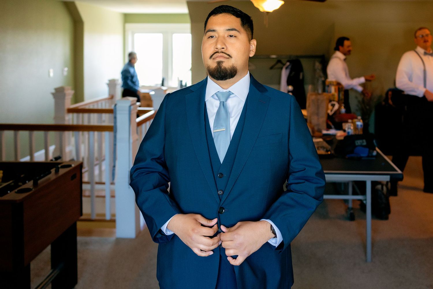 Groom in a navy blue three-piece suit buttoning his jacket while getting ready for his wedding day.