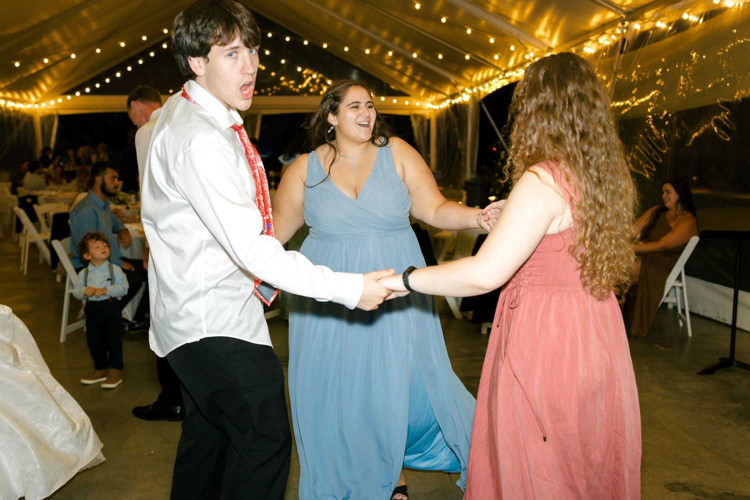 Couples dancing at wedding reception under tent with festive lighting and decorations.