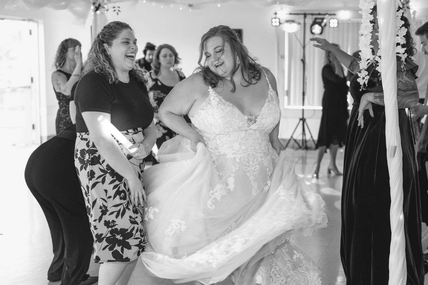 Wedding guests help adjust a flowing white dress on the dance floor.
