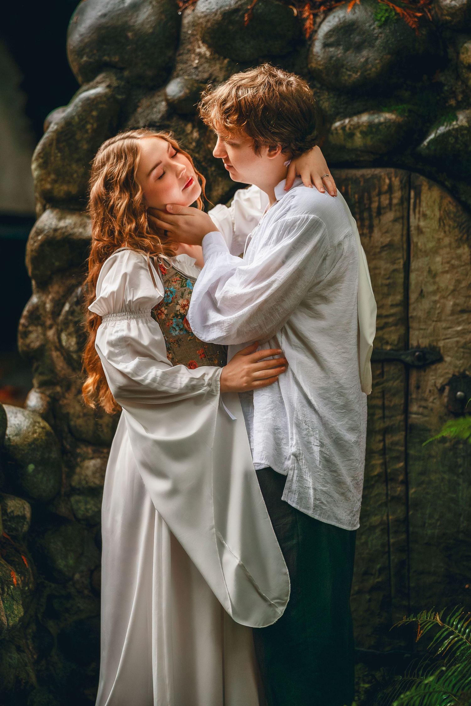 A romantic couple in white clothing embraces against a stone wall background in a series of intimate poses.