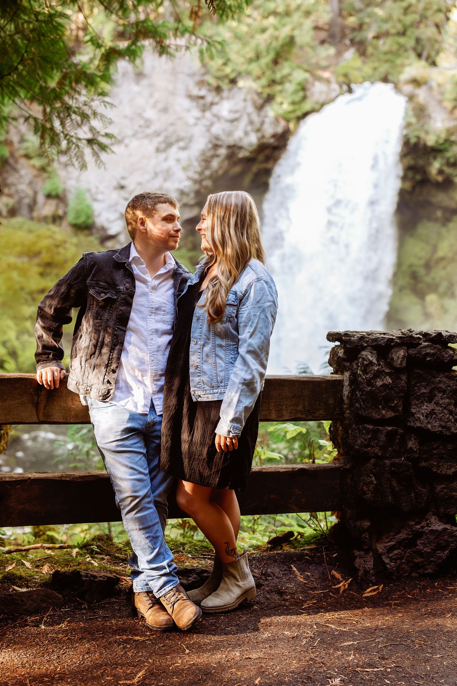 A romantic couple sits together on a wooden bench near a cascading waterfall.