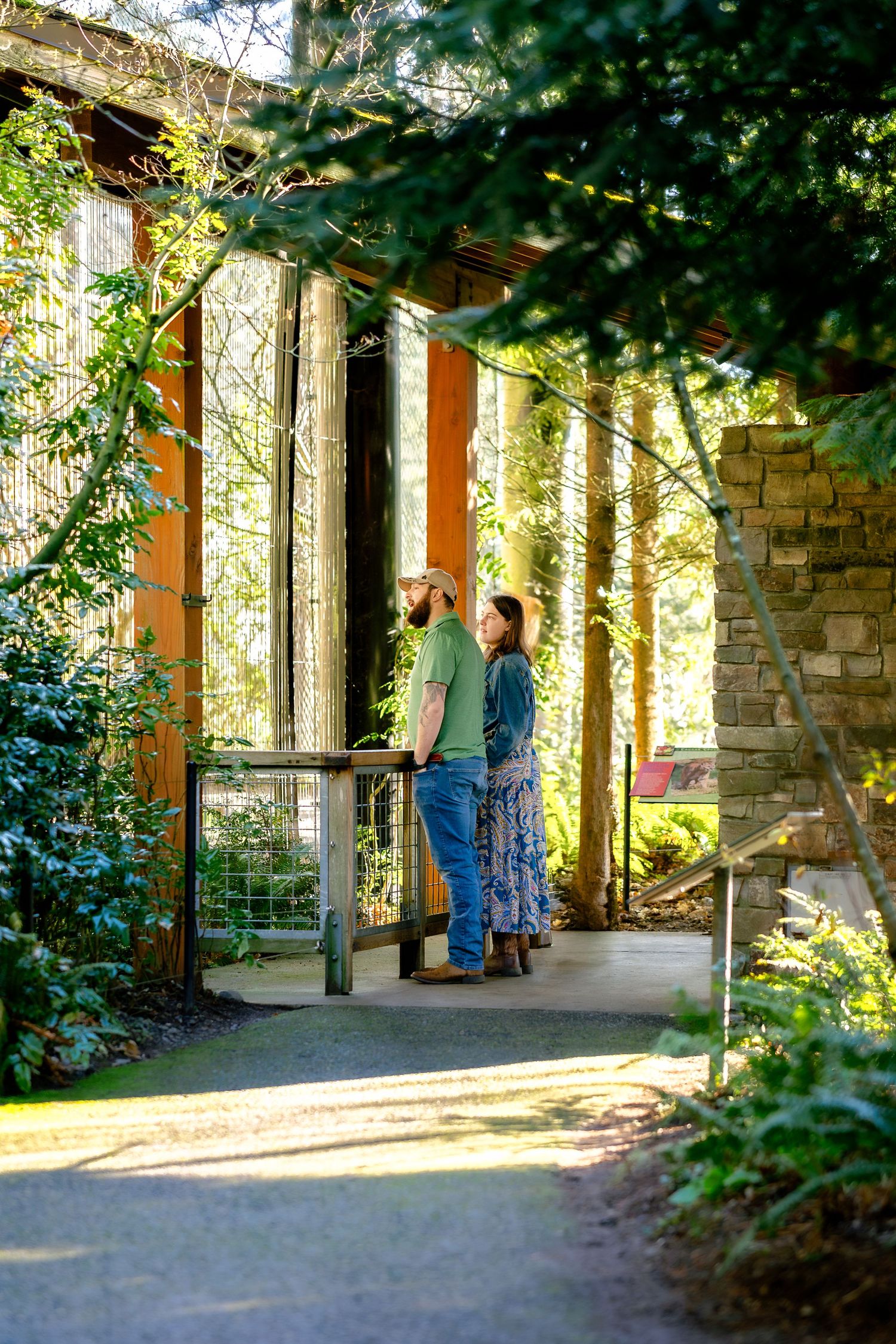 A couple stands on a stone porch with pillars surrounded by lush greenery and natural sunlight.