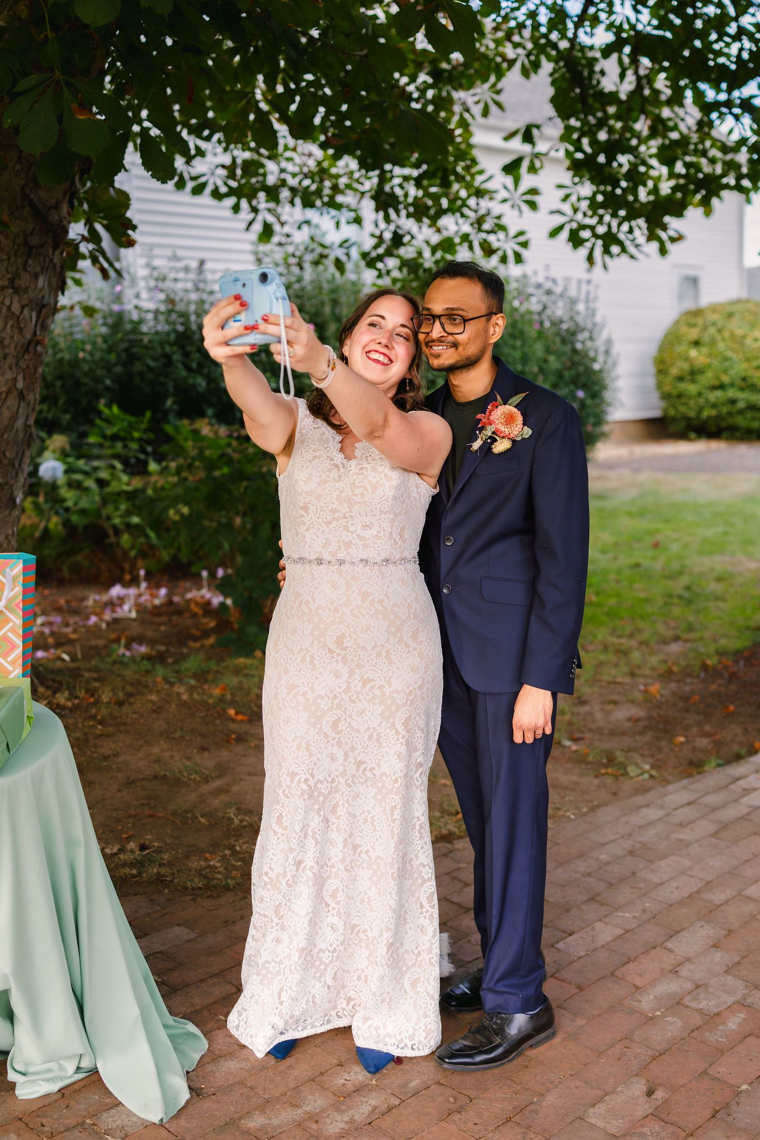 Wedding celebration on brick patio surrounded by lush green gardens and trees.