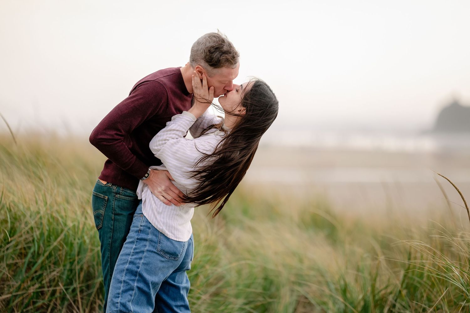 Romantic couple embraces in a misty field of tall grass during golden hour.
