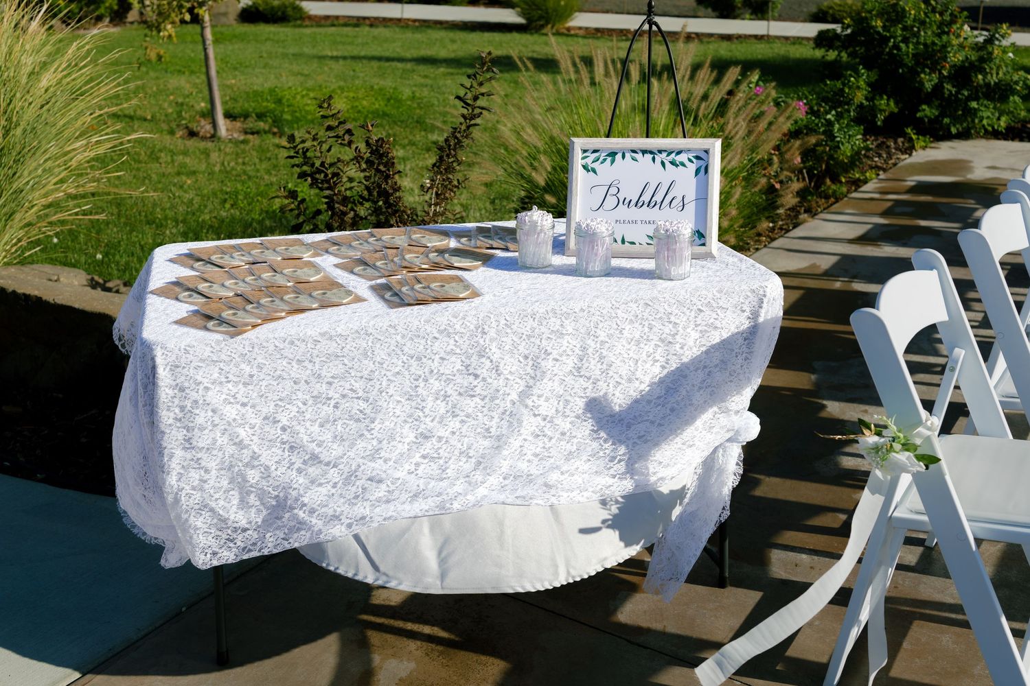 White lace tablecloths and elegant place settings arranged on outdoor tables for a garden wedding reception.
