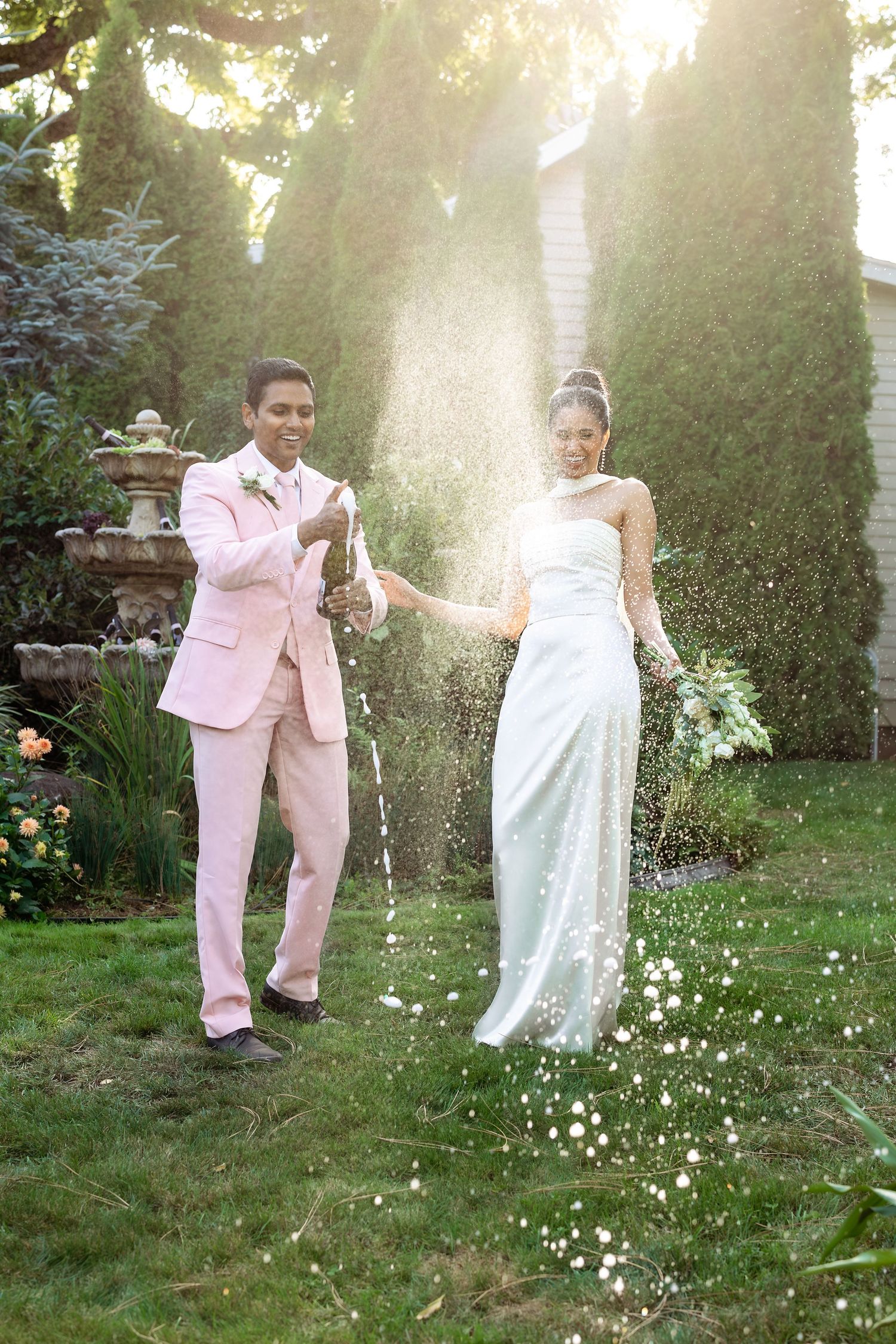 Wedding couple celebrating with champagne in a sunlit garden.