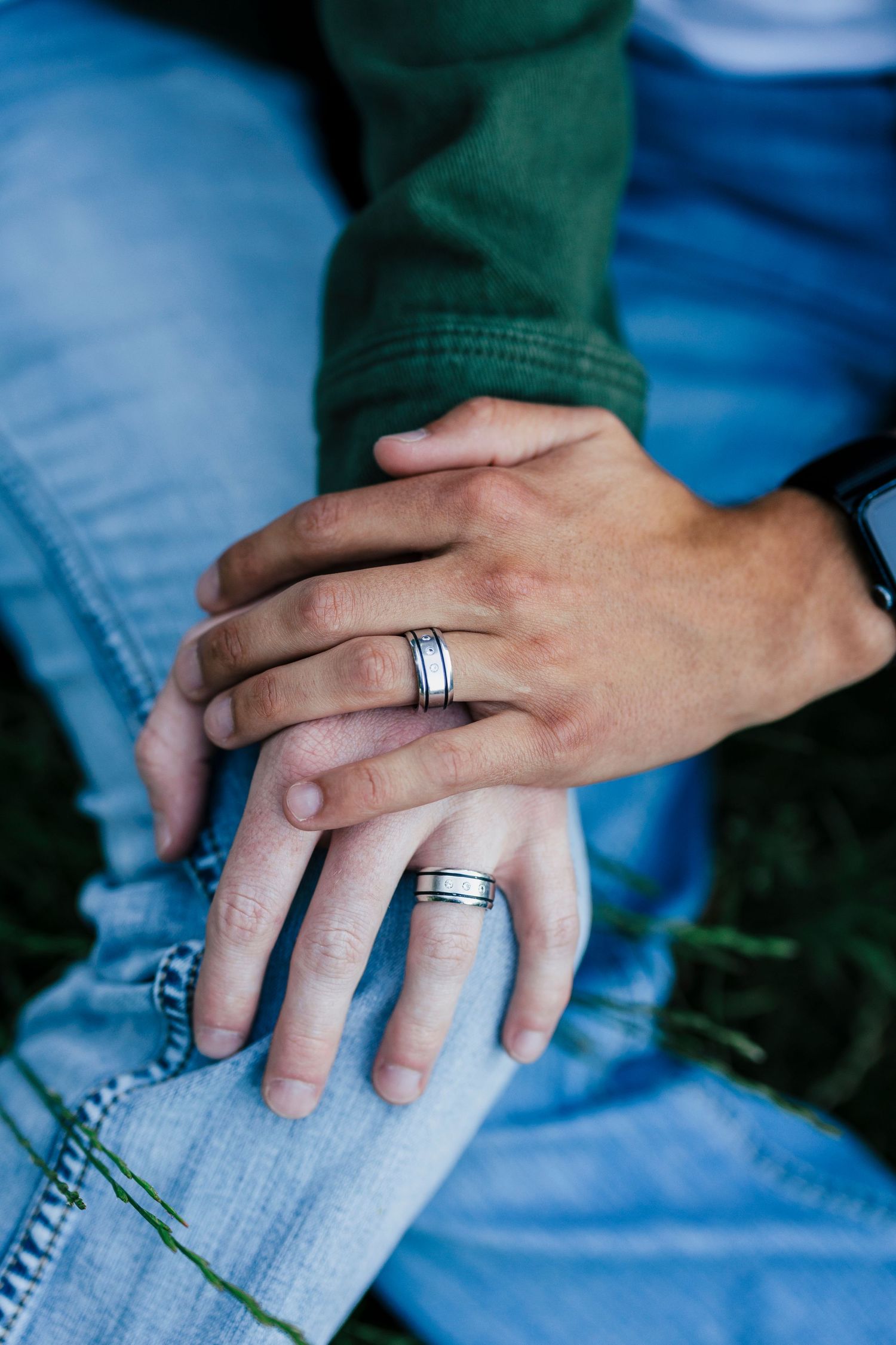 Close up shot of two hands with matching silver wedding bands resting on blue denim jeans.
