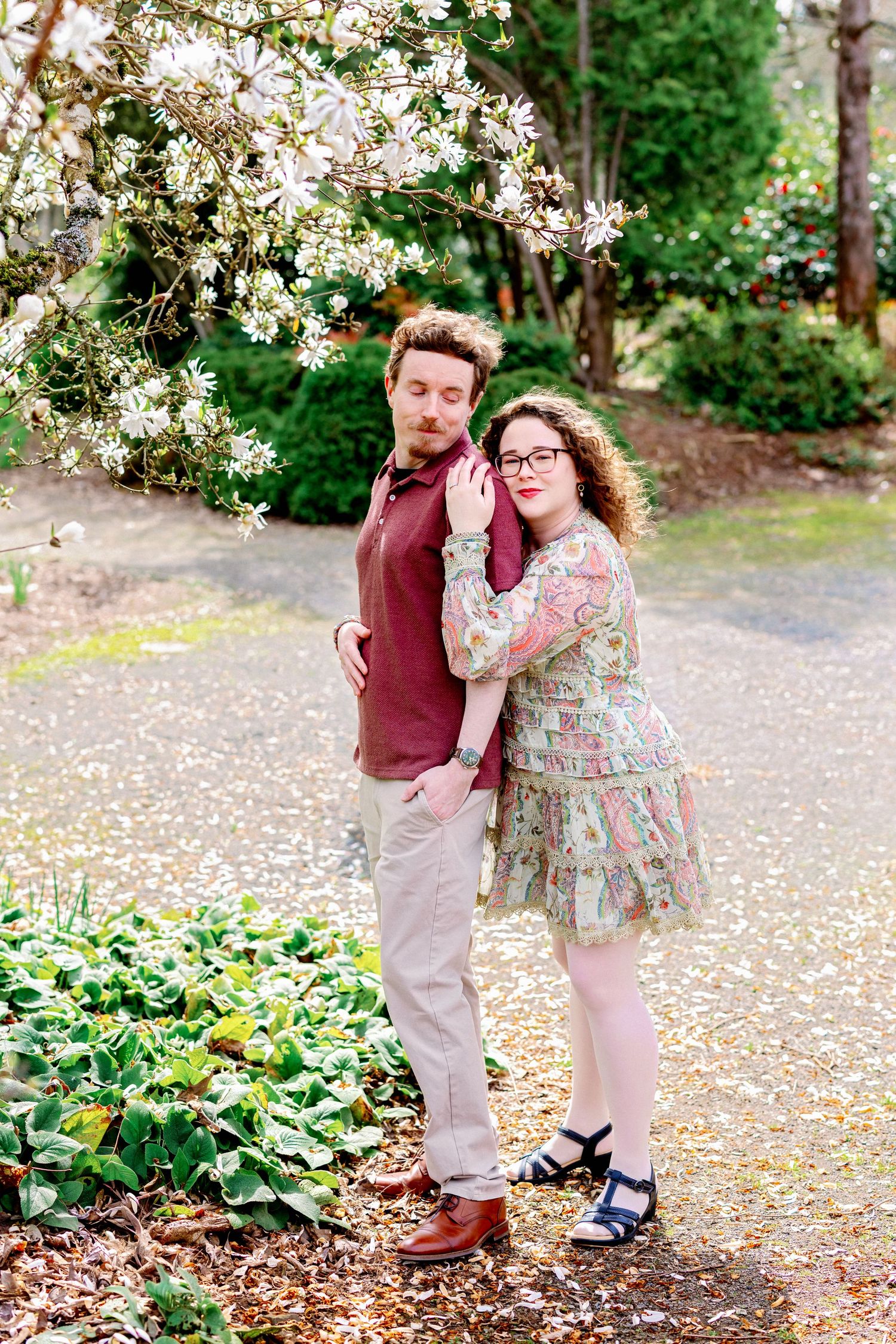 Couple sharing romantic moments under blooming cherry blossoms in a garden setting with scattered petals.
