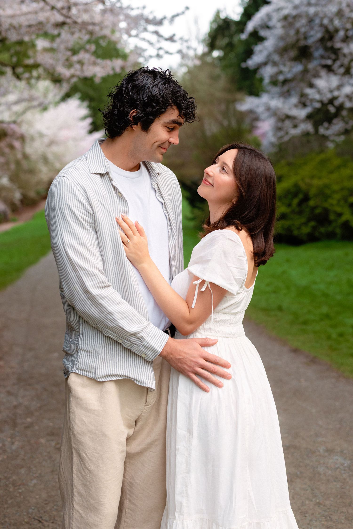 A couple shares a romantic moment under blooming cherry blossom trees on a spring path.