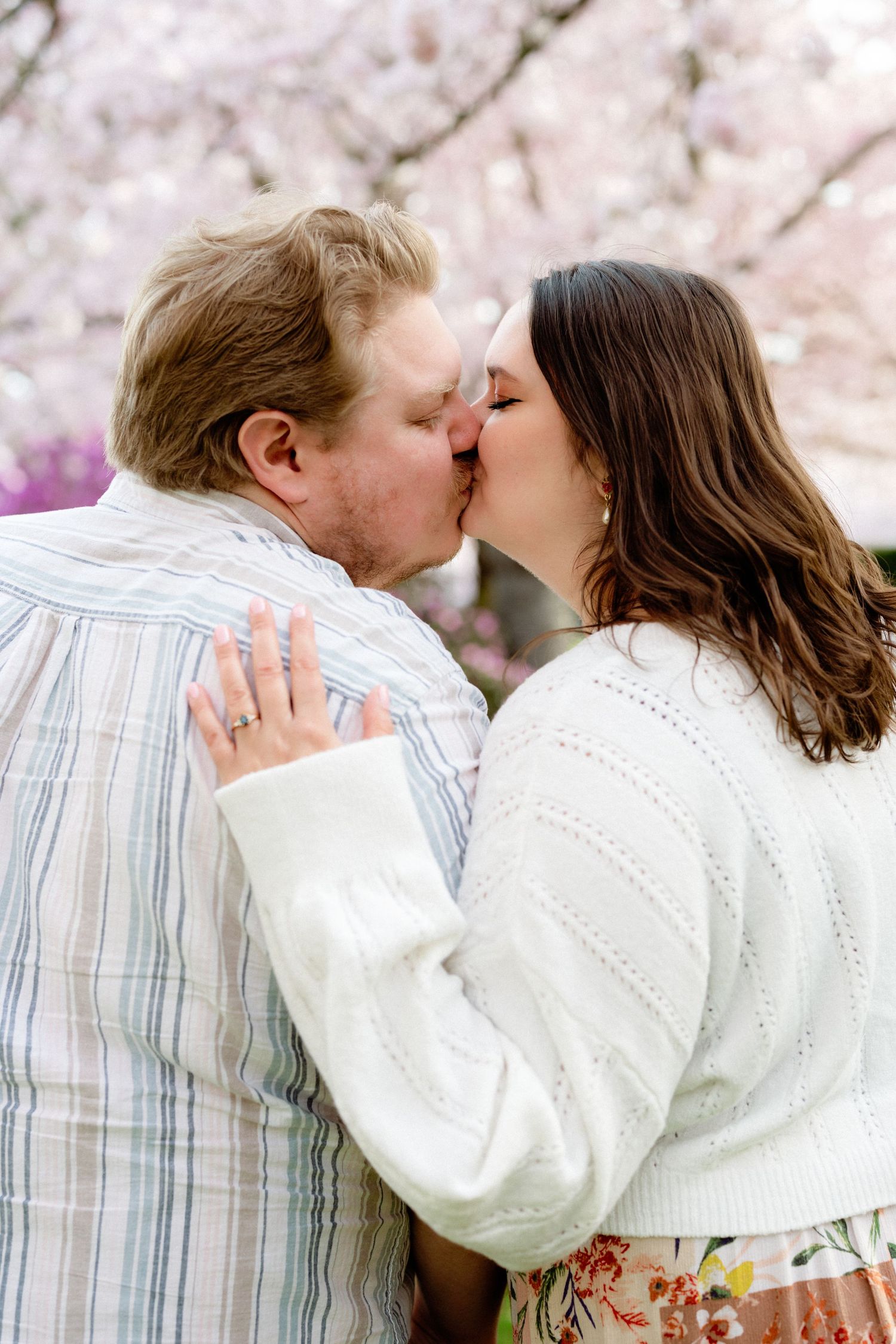 A romantic moment shared under flowering cherry blossom trees in springtime.