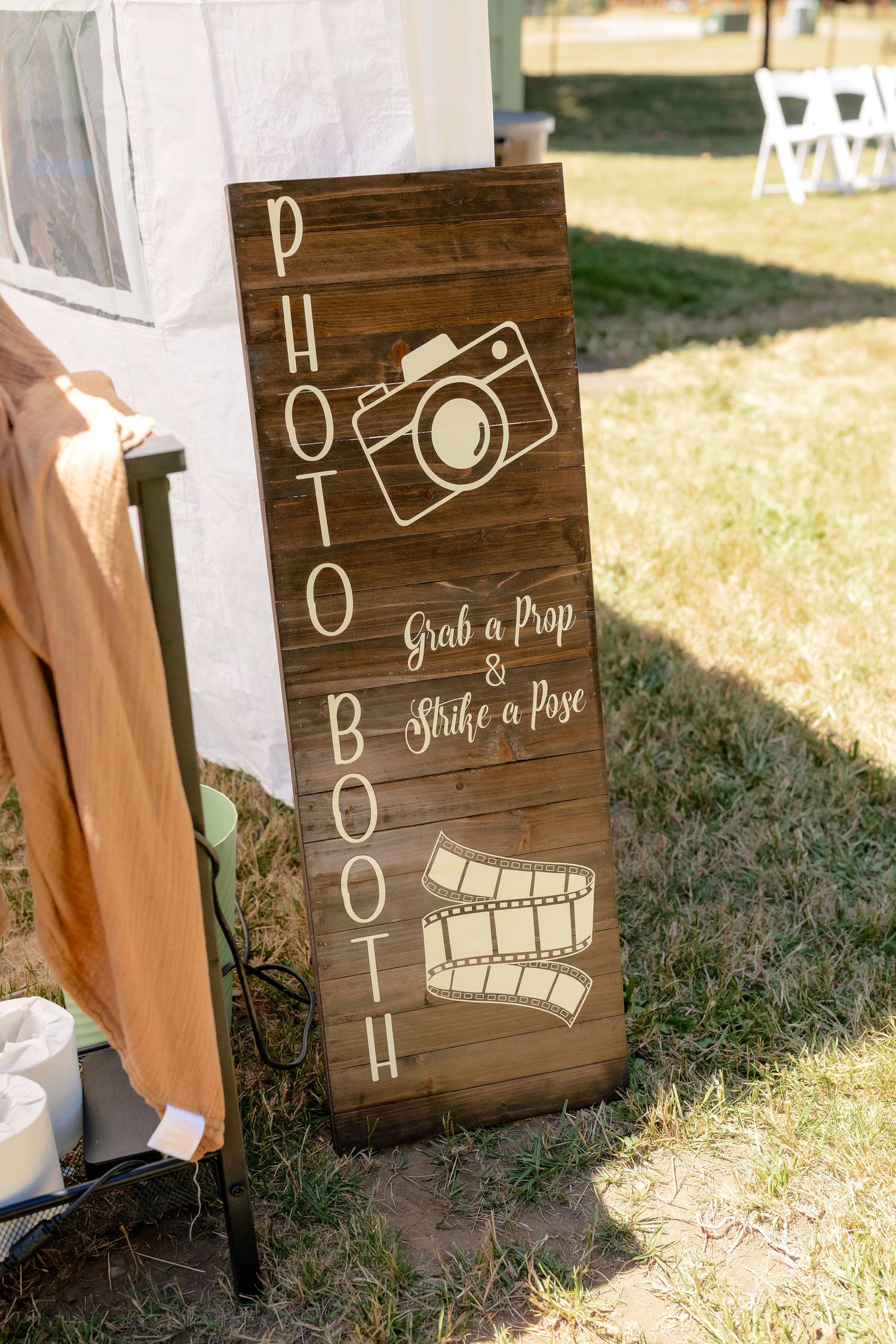 Wooden photo booth sign with camera and film reel icons reading Grab a Prop and Strike a Pose outdoors.