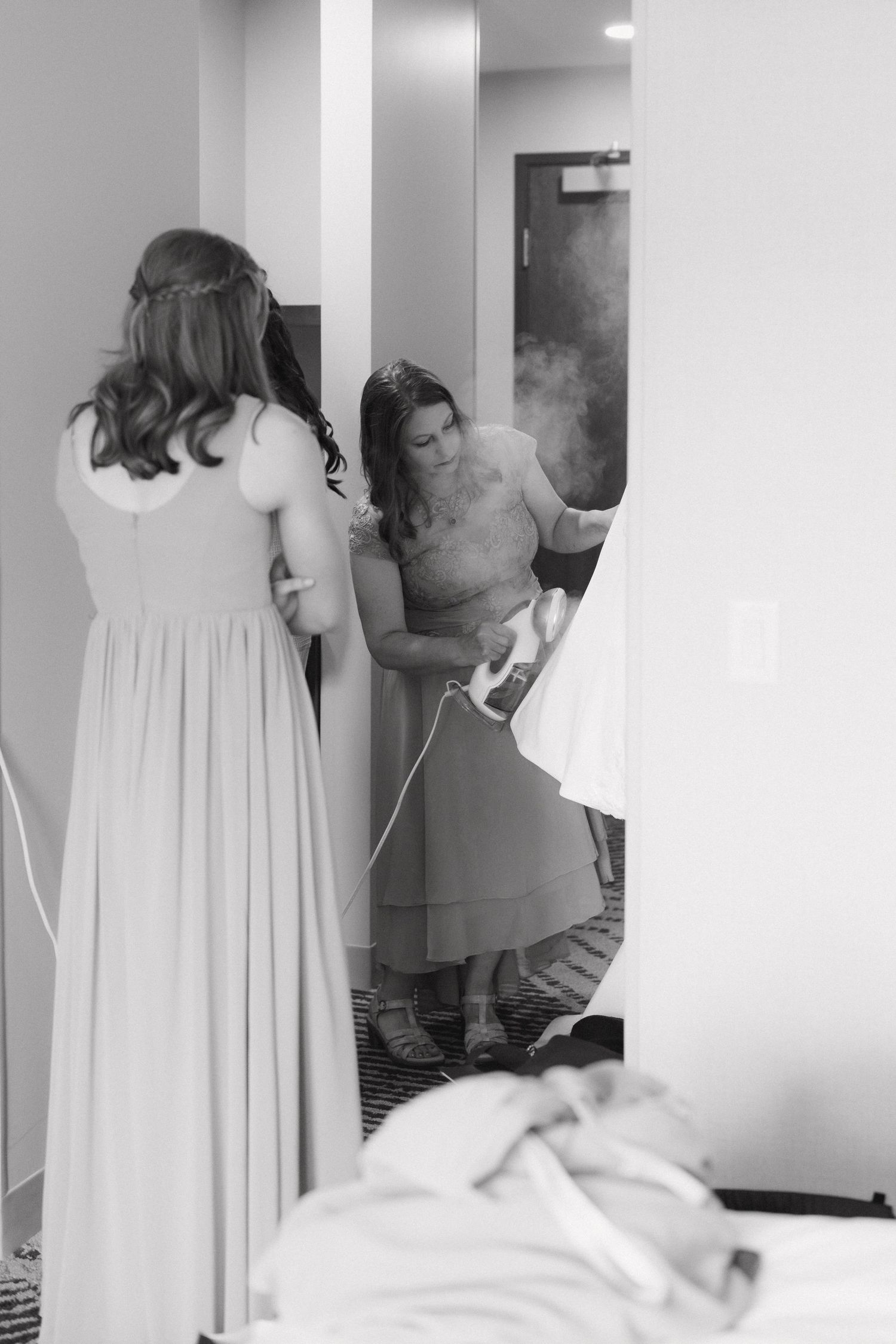 Bridesmaid steaming a wedding dress in a hotel room in black and white photo.
