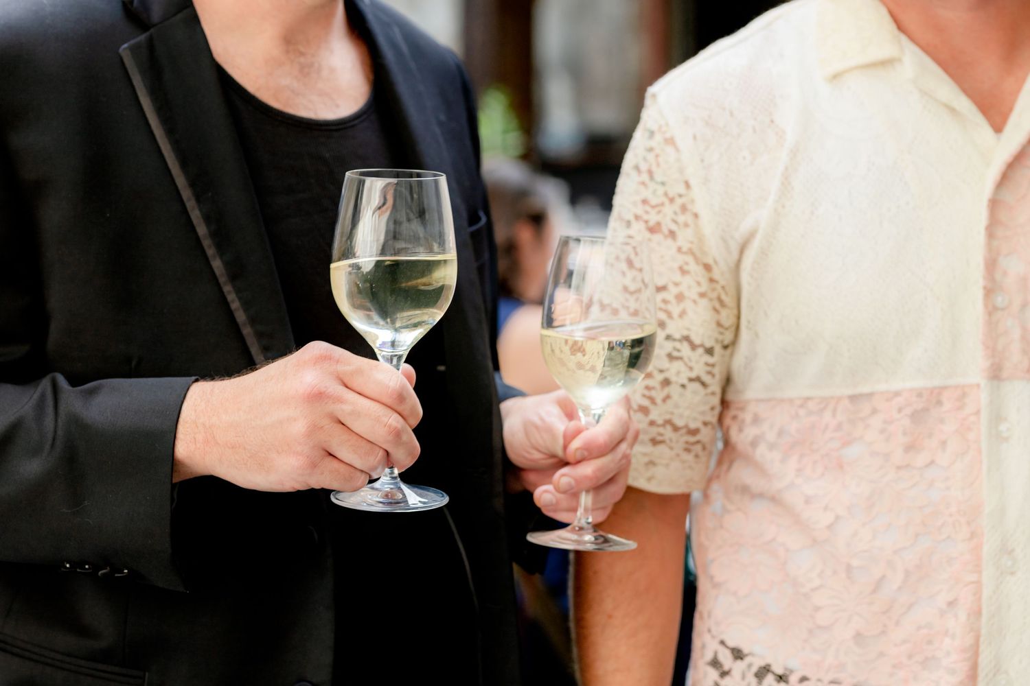 Two guests holding white wine glasses at an outdoor wedding reception.